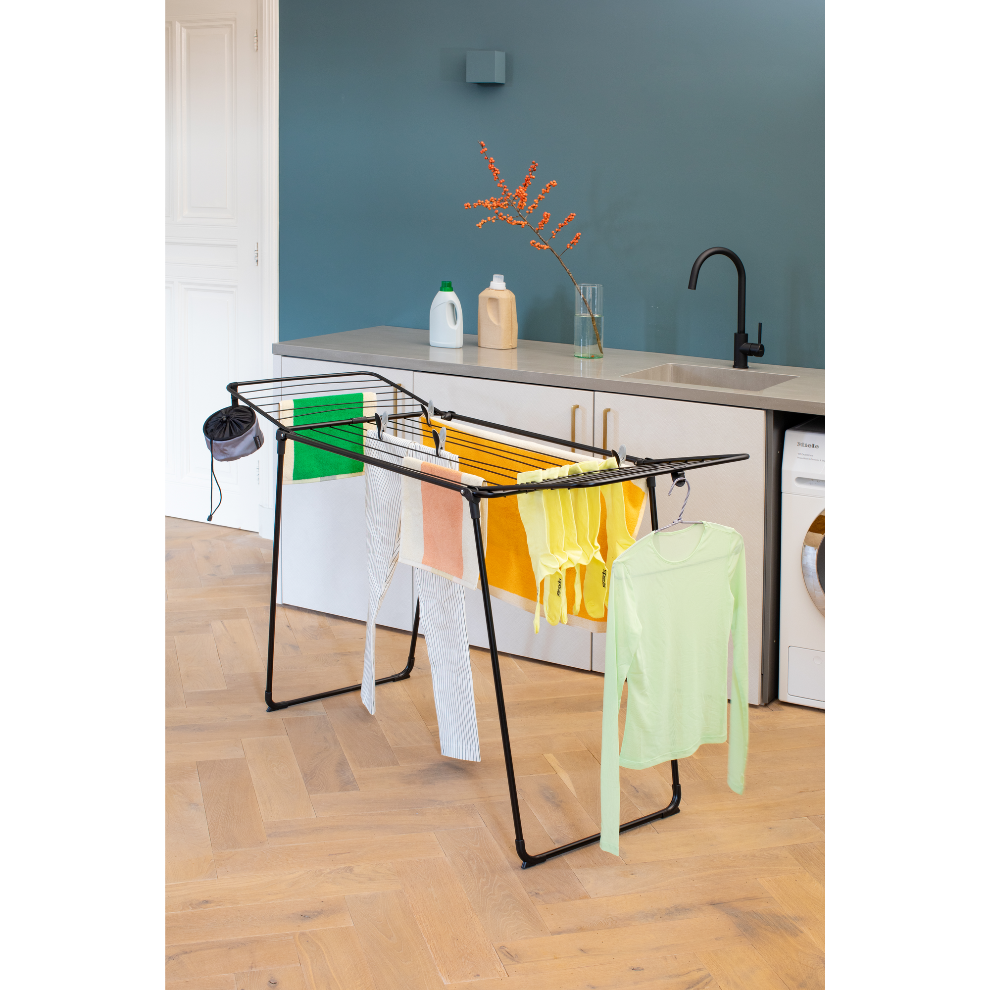 A black clothes drying rack with colorful laundry stands on a wooden floor.