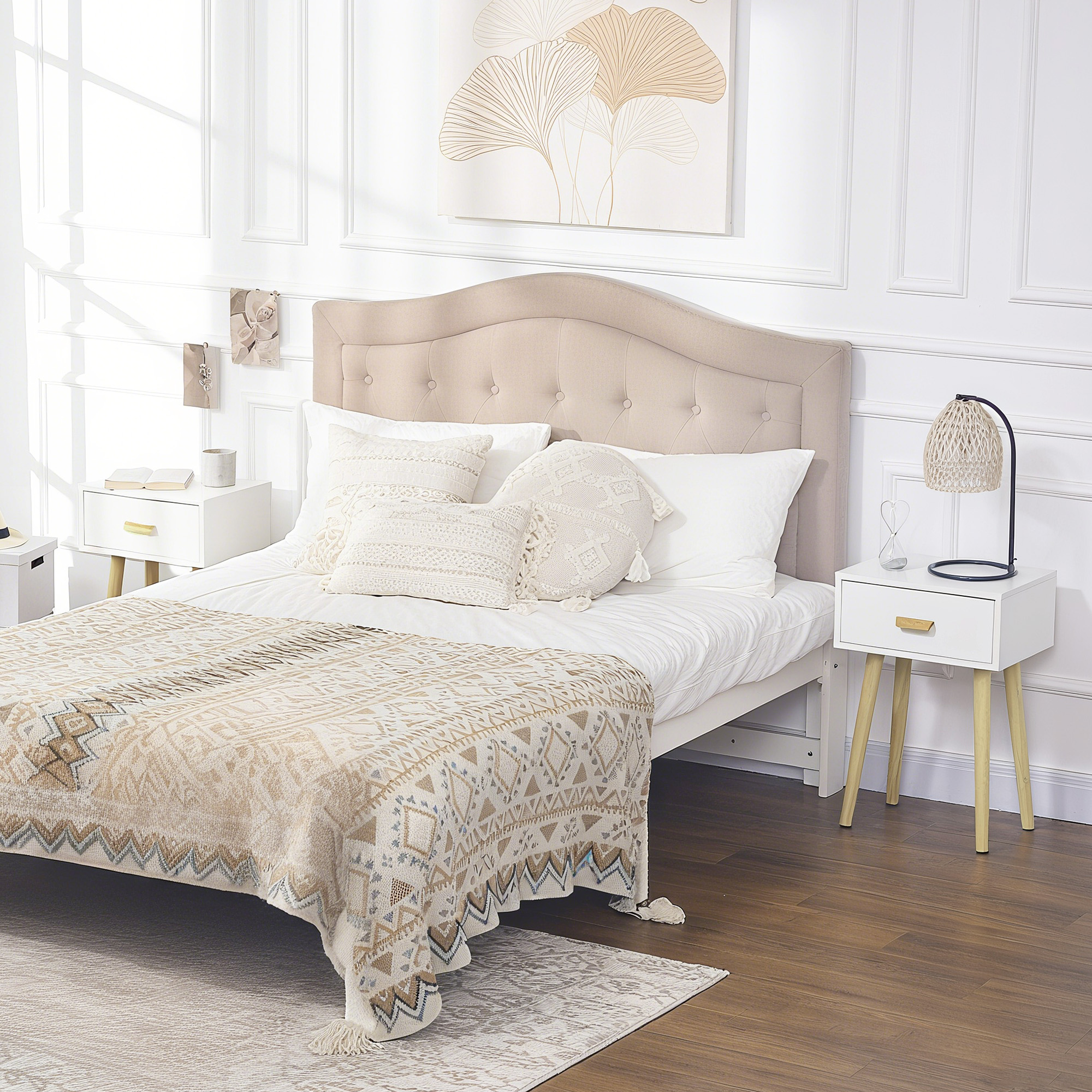 Un dormitorio con cama beige de cabecero tapizado, almohadas blancas y manta estampada.
