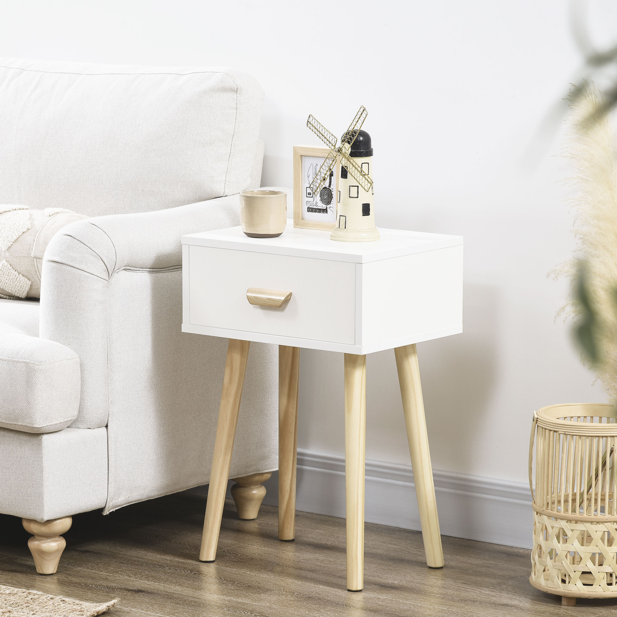 Una mesita de noche blanca con cajón se sienta junto a un sofá. Decoraciones sobre la mesa.