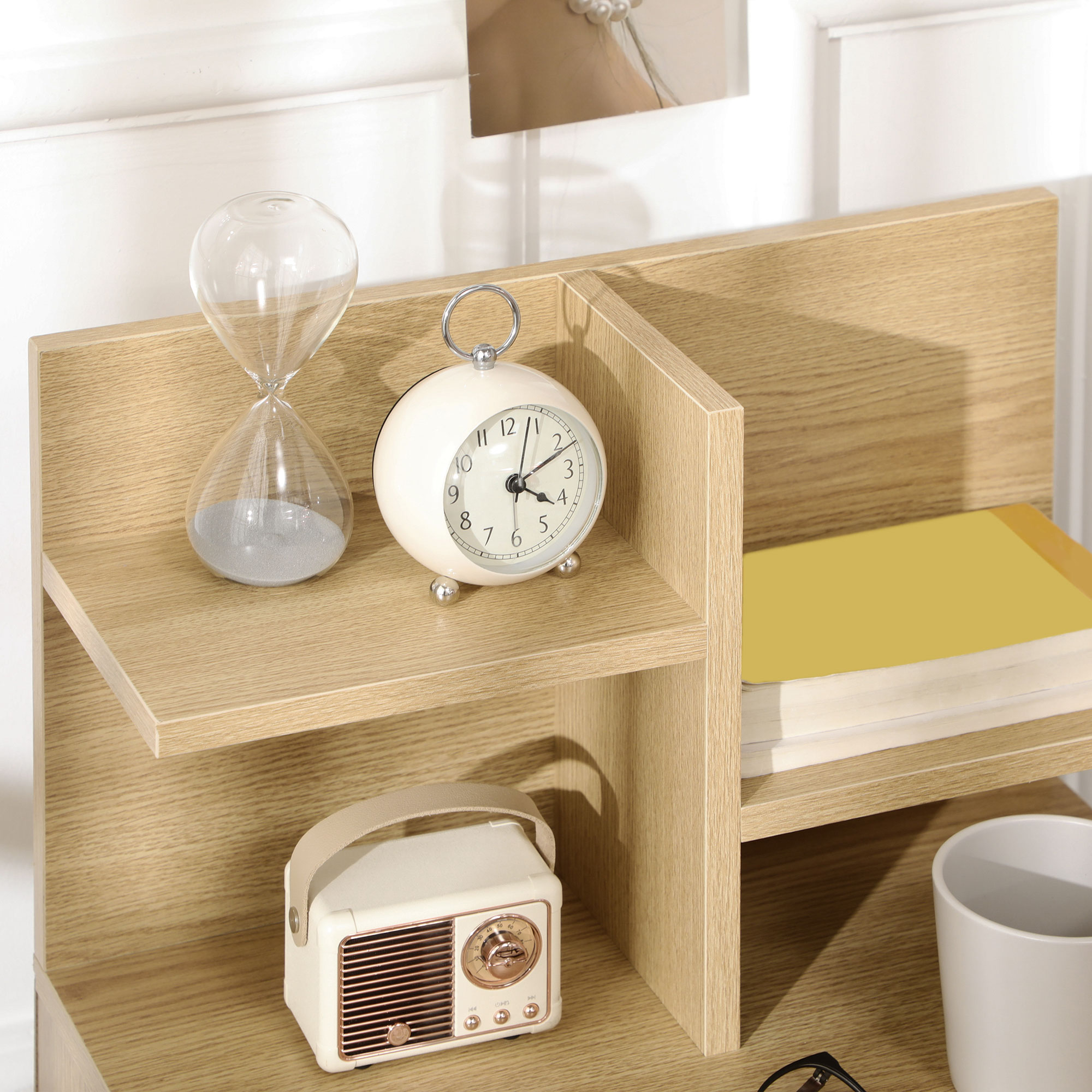 Una estantería de madera tiene un reloj de arena, despertador, radio, libros y taza.
