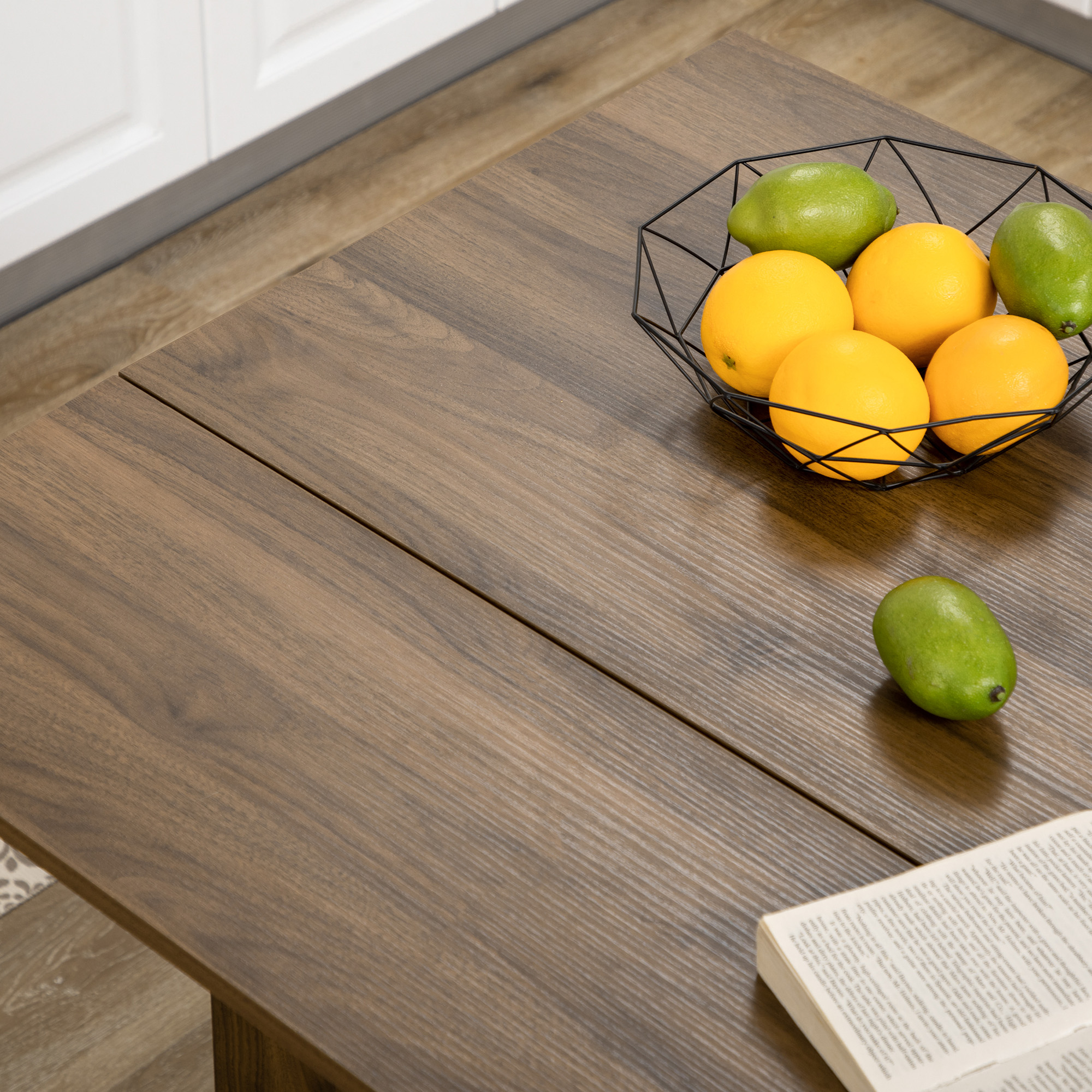 Una cesta de alambre negra con naranjas y frutas verdes sobre una mesa de madera.