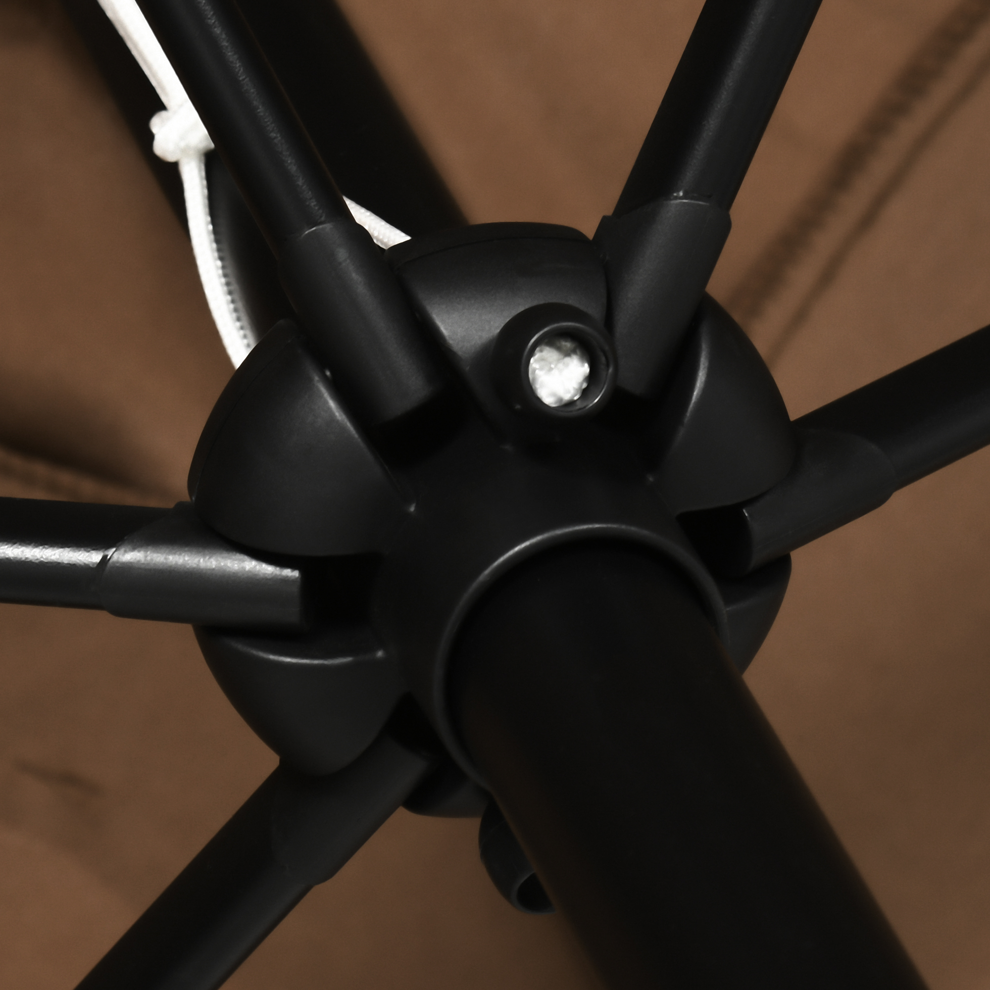 Primo piano dell'articolazione centrale di un ombrello nero con corde bianche e sfondo marrone.