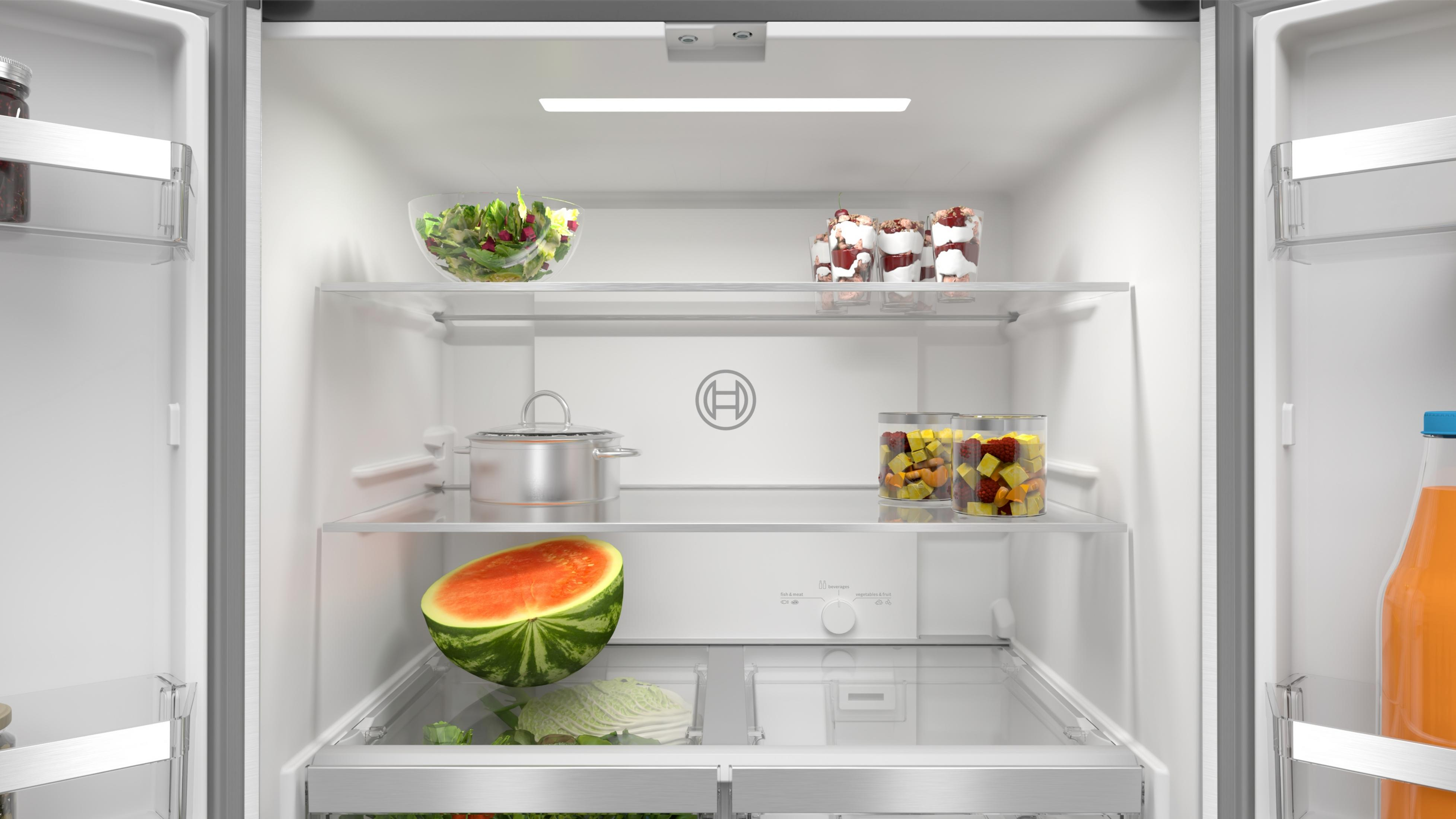 Otwarta lodówka z sałatką, deserami w szklankach, garnkiem, połówką arbuza, kapustą i sokiem.
