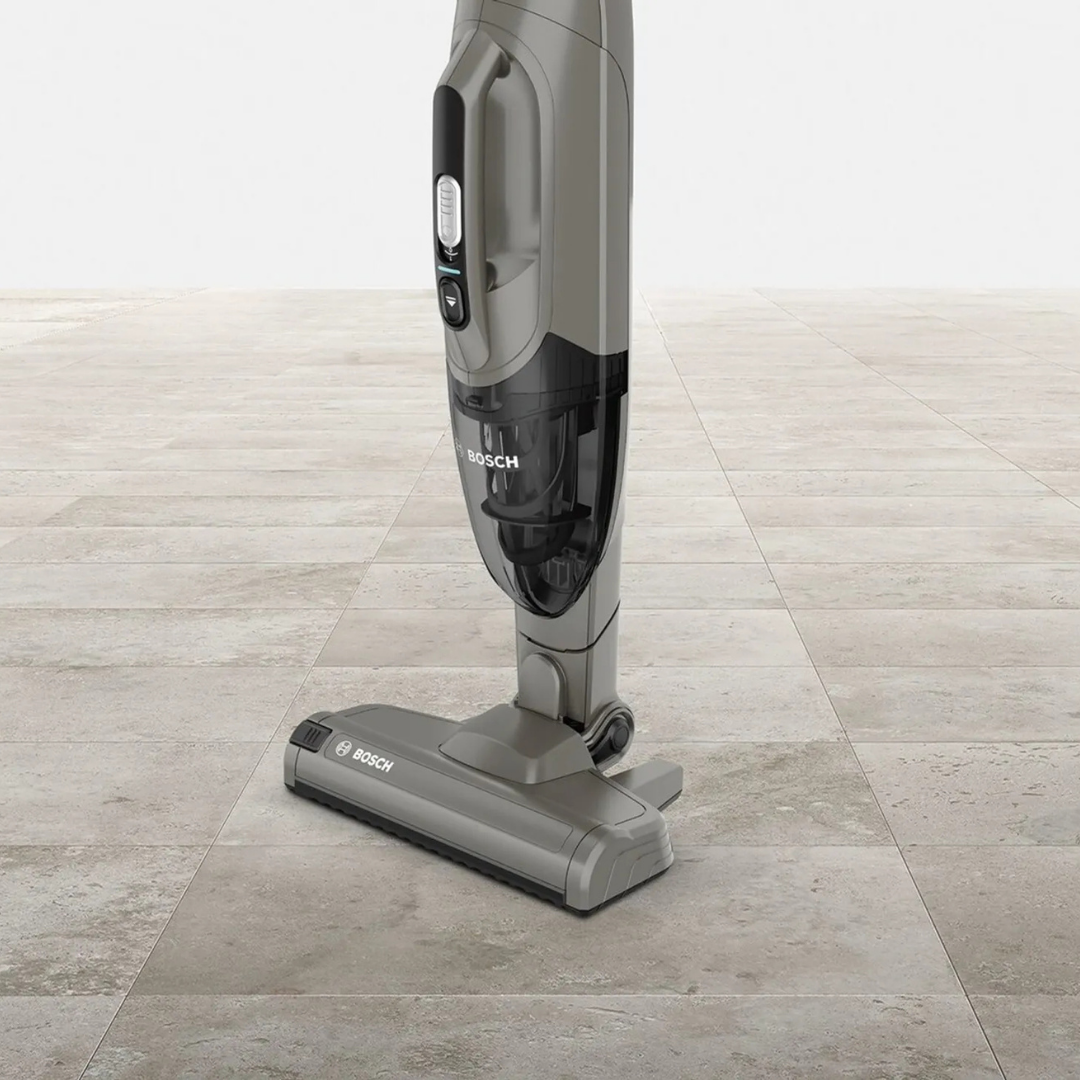 Szary odkurzacz bezprzewodowy z przezroczystym pojemnikiem na kurz na podłodze z płytek.