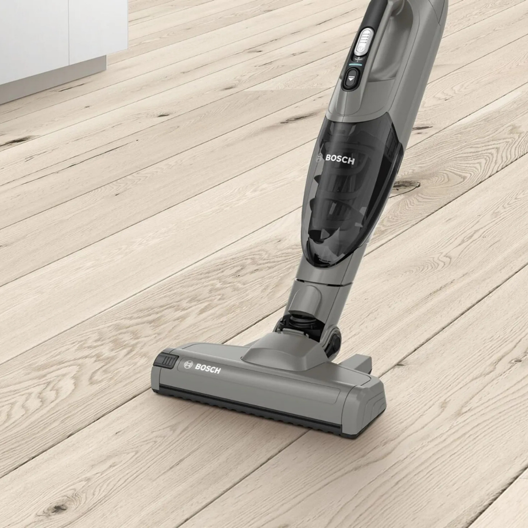 Szary odkurzacz akumulatorowy Bosch na jasnej drewnianej podłodze.
