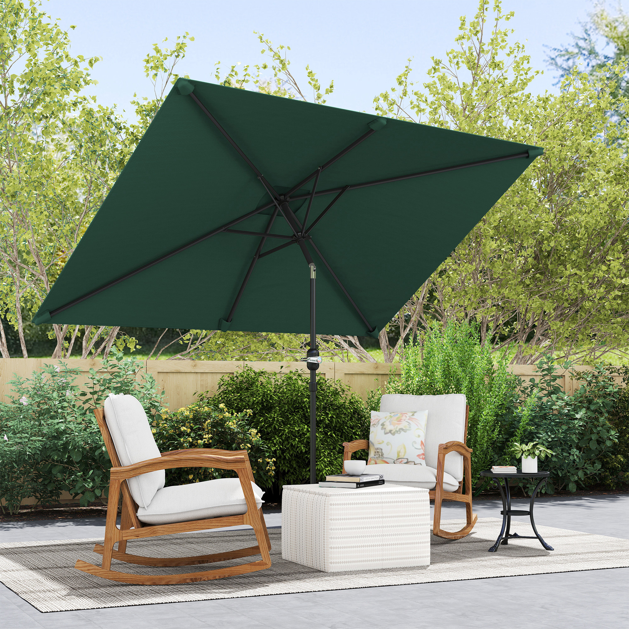 Due sedie a dondolo sotto un grande ombrellone verde su un patio con lussureggianti cespugli verdi.