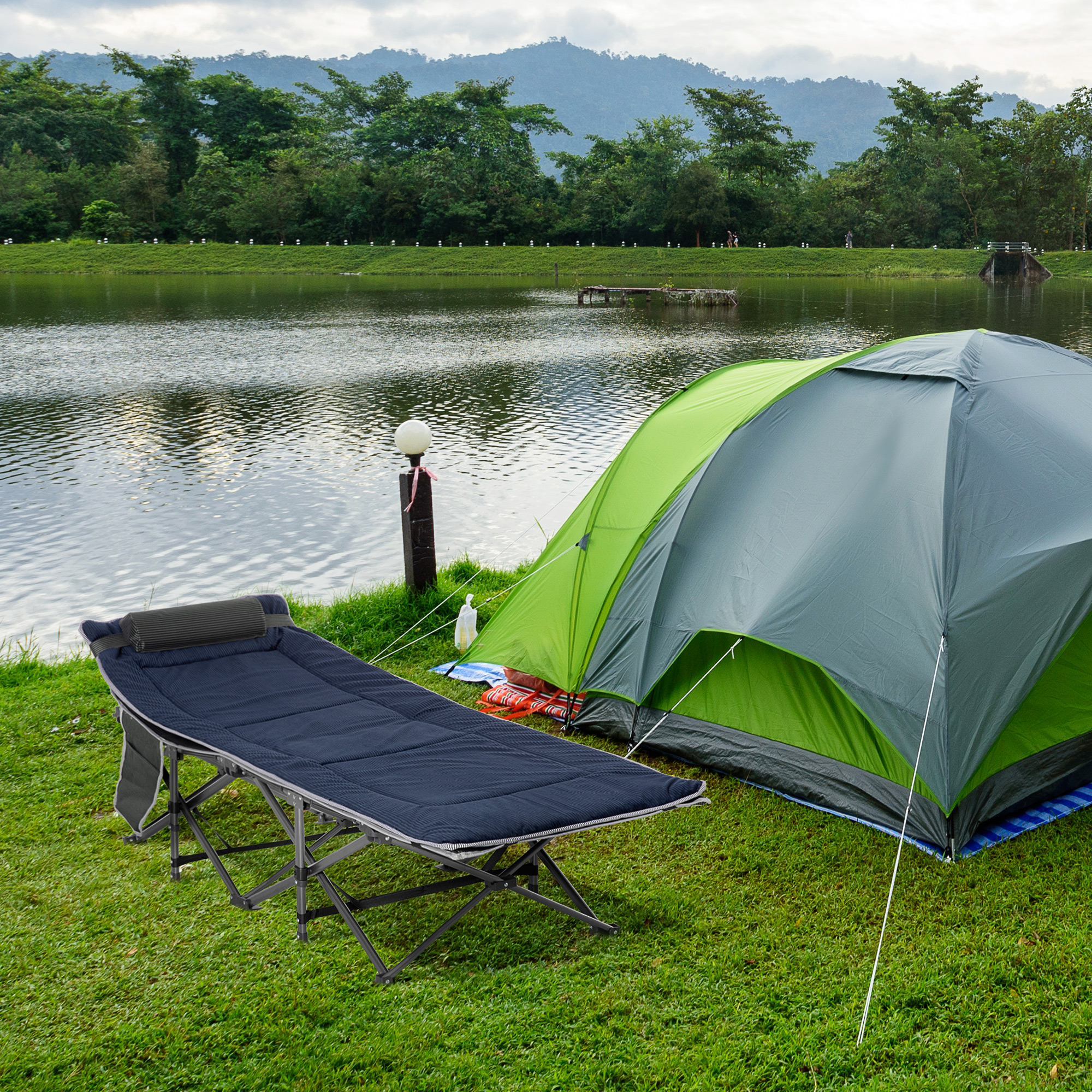 Un camping junto a un lago con tienda, cama de campaña y montañas.
