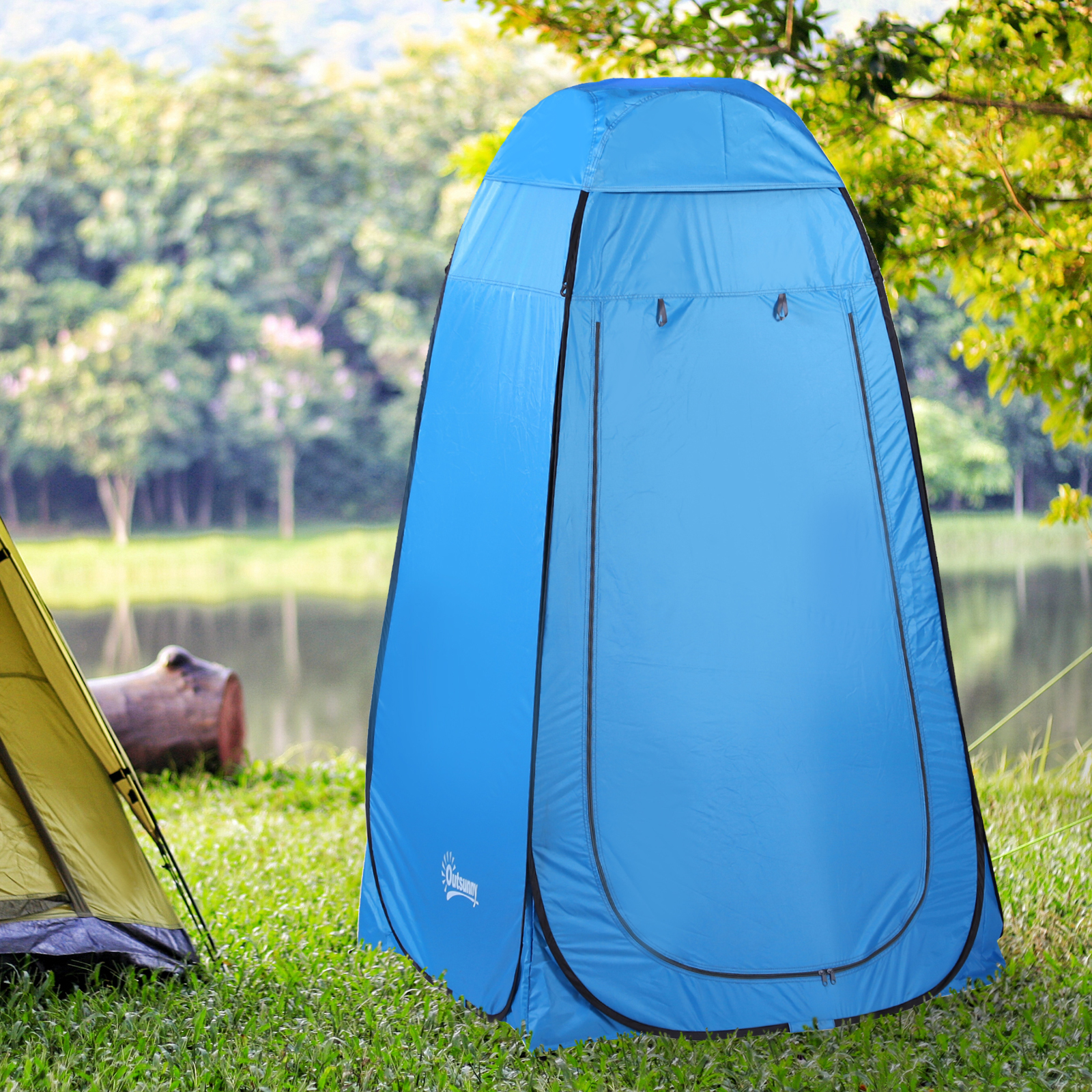 Una carpa azul está en la hierba junto a una carpa amarilla, con árboles y un lago al fondo.
