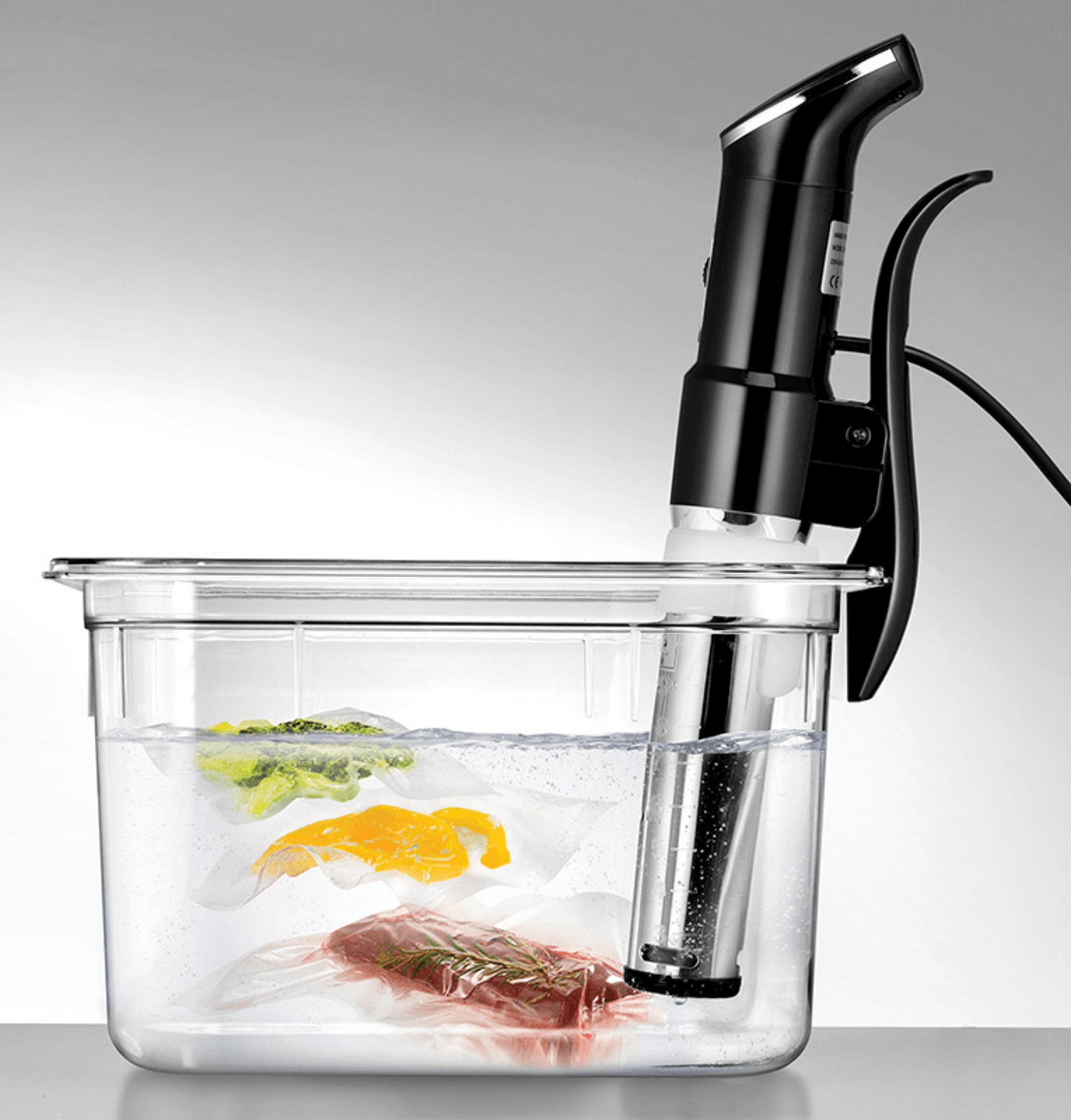 Ein Sous-vide-Garer in einem Wasserbad mit vakuumverpacktem Fleisch und Gemüse.