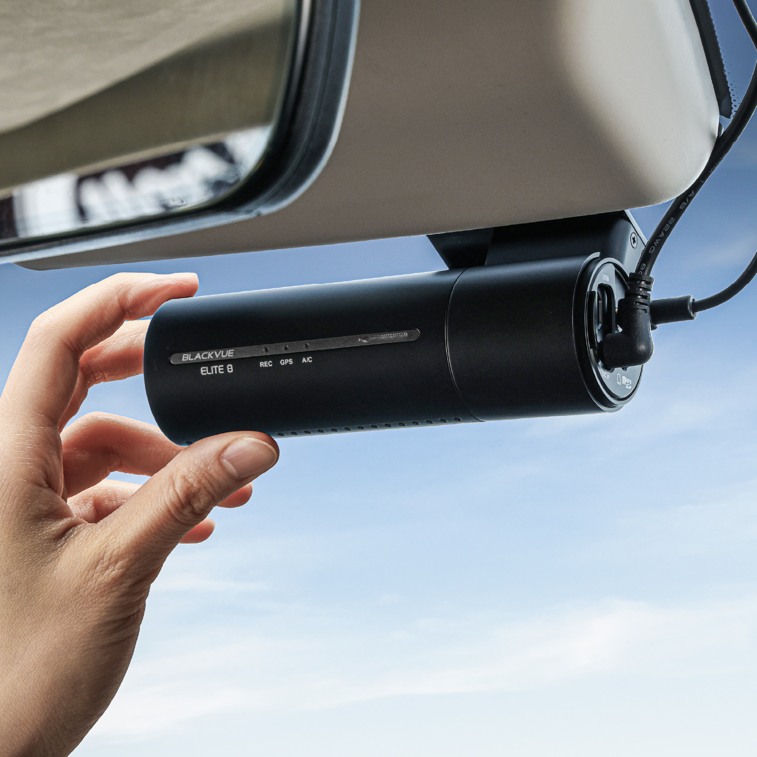 Een hand houdt een zwarte Blackvue Elite 8 dashcam vast tegen een blauwe lucht.