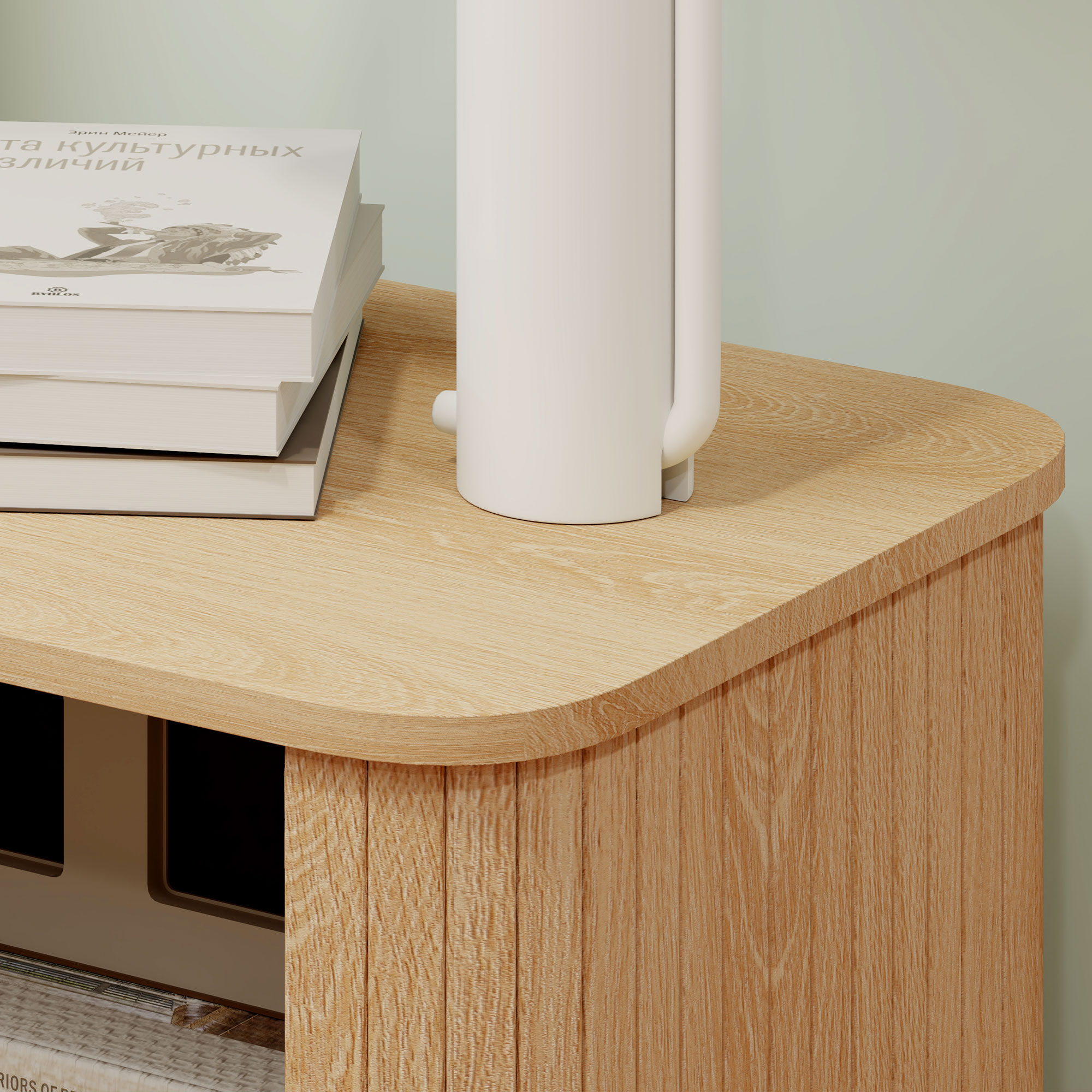 Un hervidor blanco y una pila de libros sobre una mesa de madera contra una pared verde pálido.