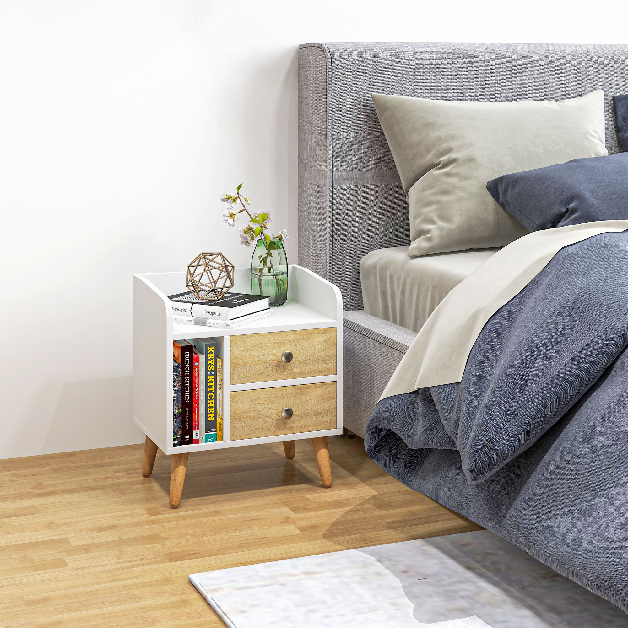 Una mesita de noche blanca con libros y decoración junto a una cama con almohadas azules y grises.