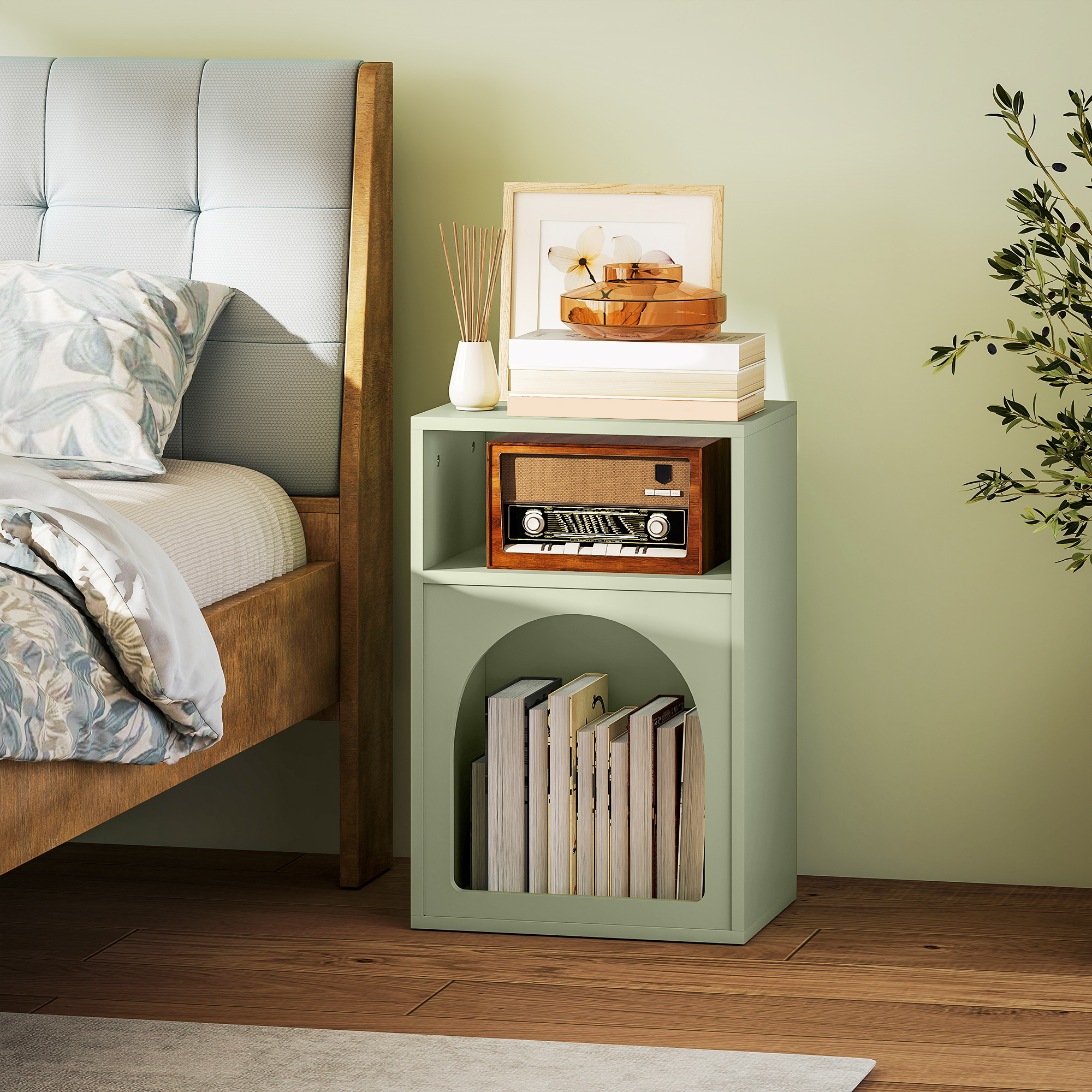 Mesita de noche de madera con radio y libros. Al lado hay una cama.