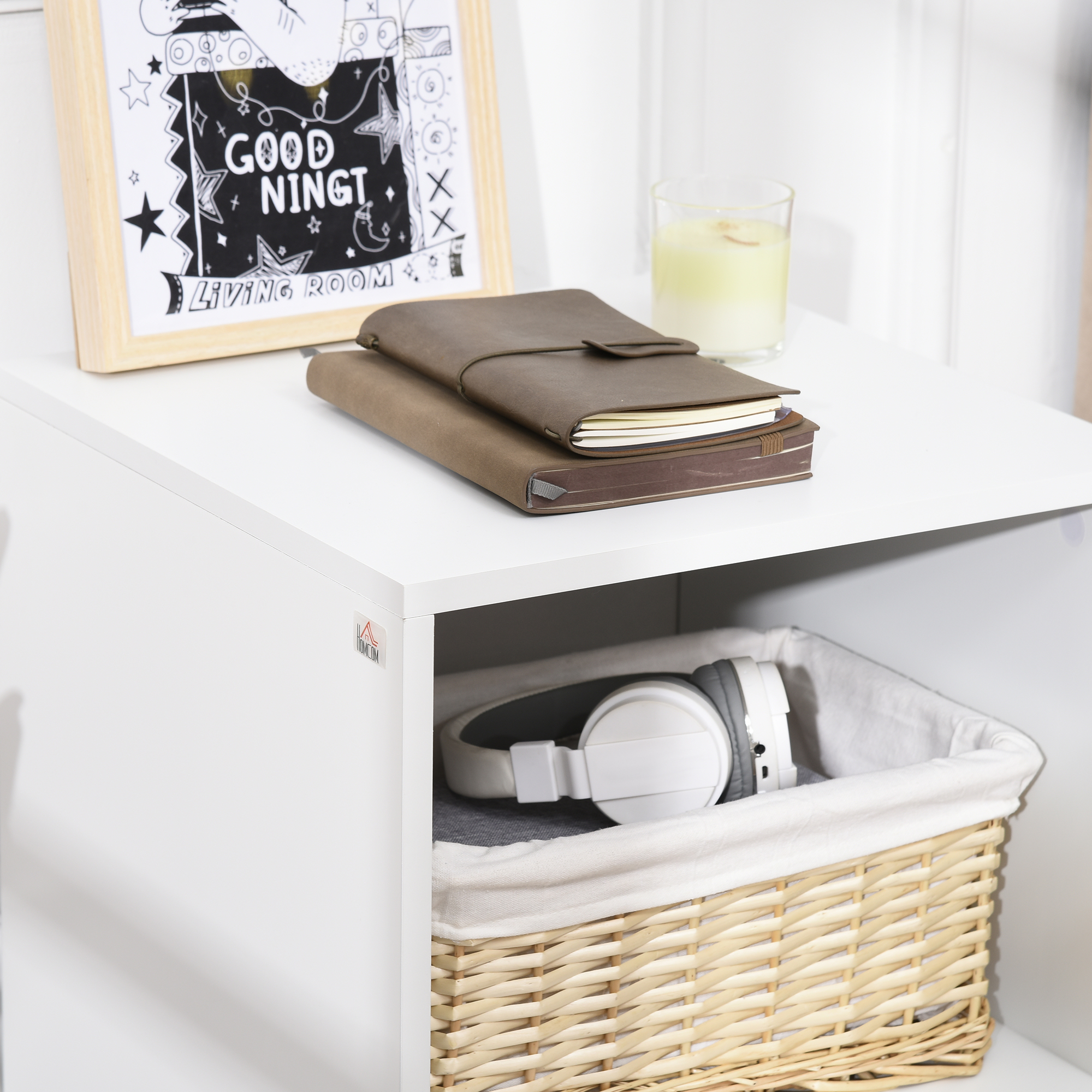 Un estante blanco con libros, una vela y auriculares en una cesta.