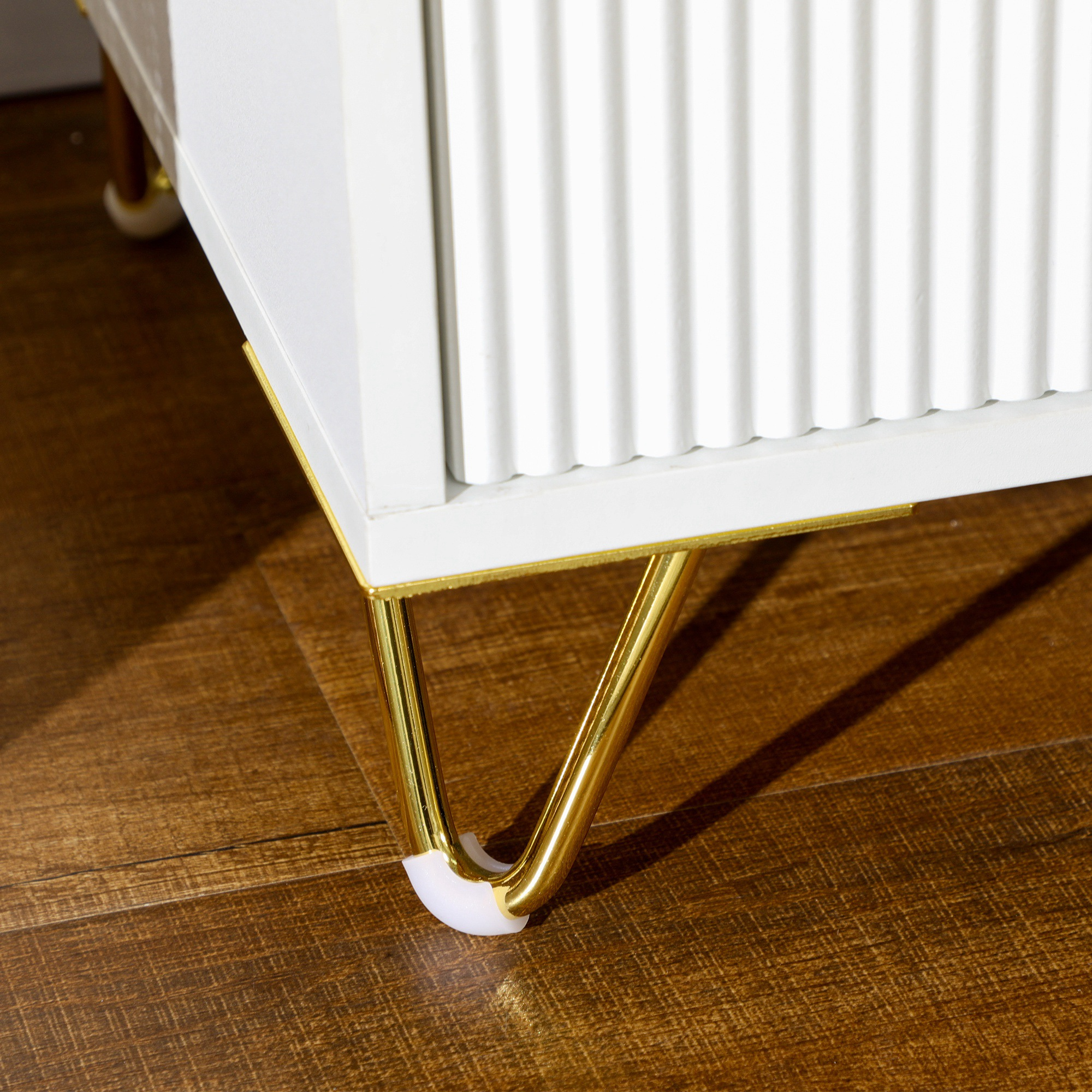 Primer plano de patas de mueble blancas con ribete dorado sobre suelo de madera.