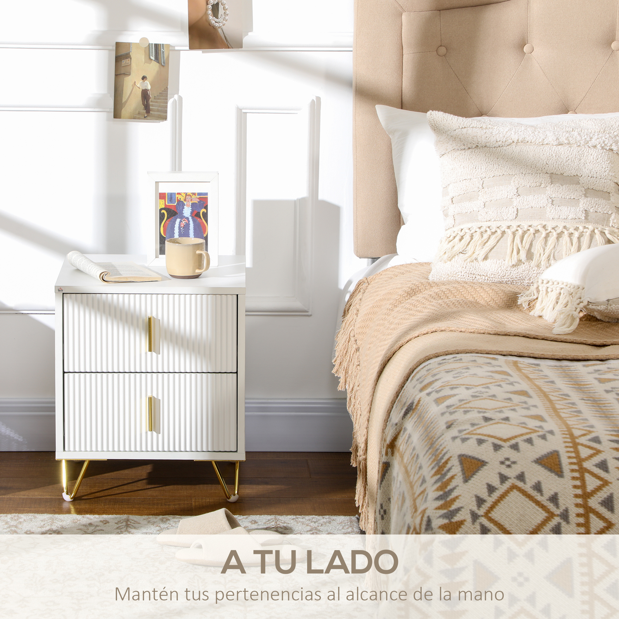 Una mesita de noche blanca con dos cajones y tiradores dorados junto a una cama.