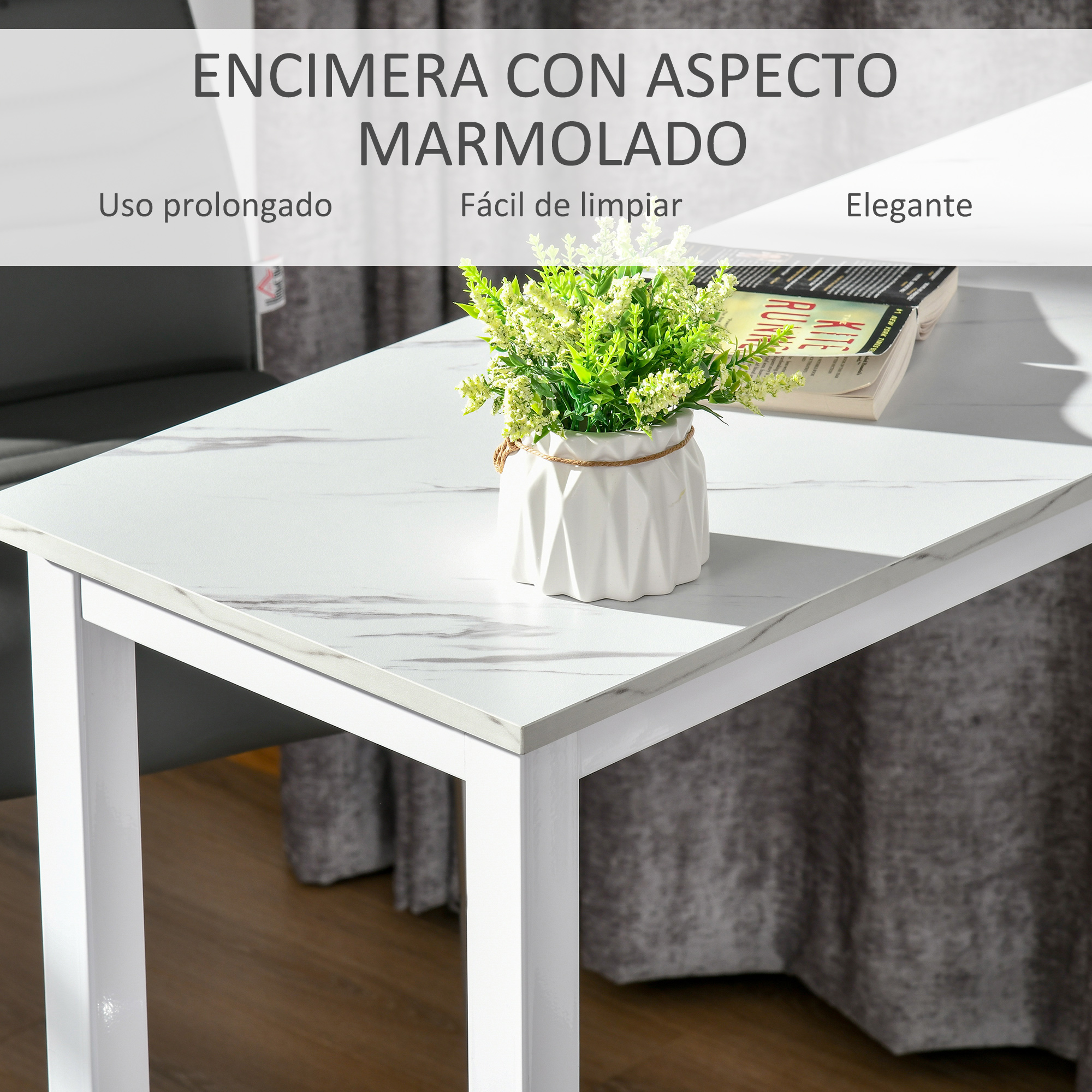 Una mesa blanca con aspecto de mármol, con un jarrón de plantas verdes y un libro.