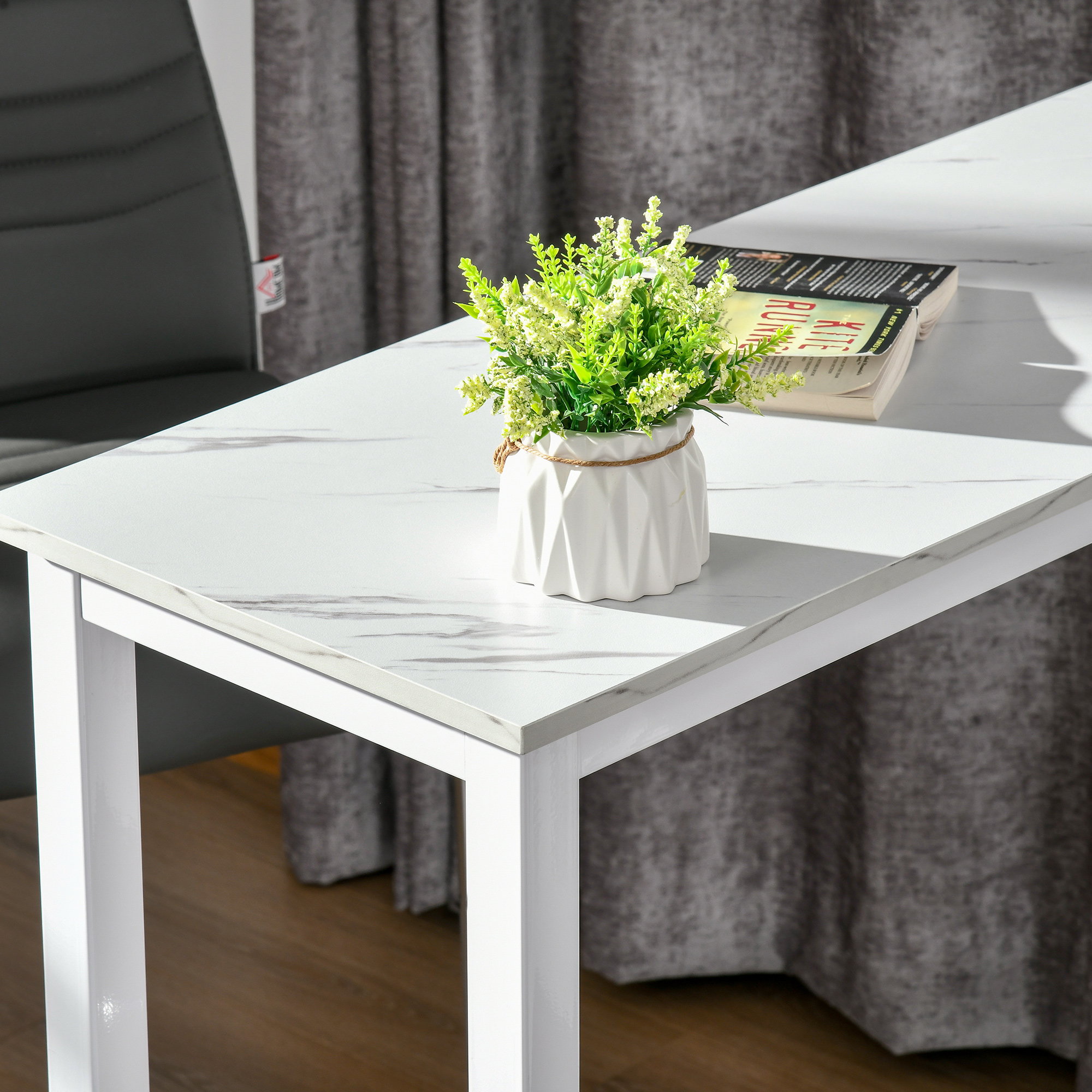 Una maceta blanca con plantas verdes sobre una mesa de mármol. Un libro al lado.