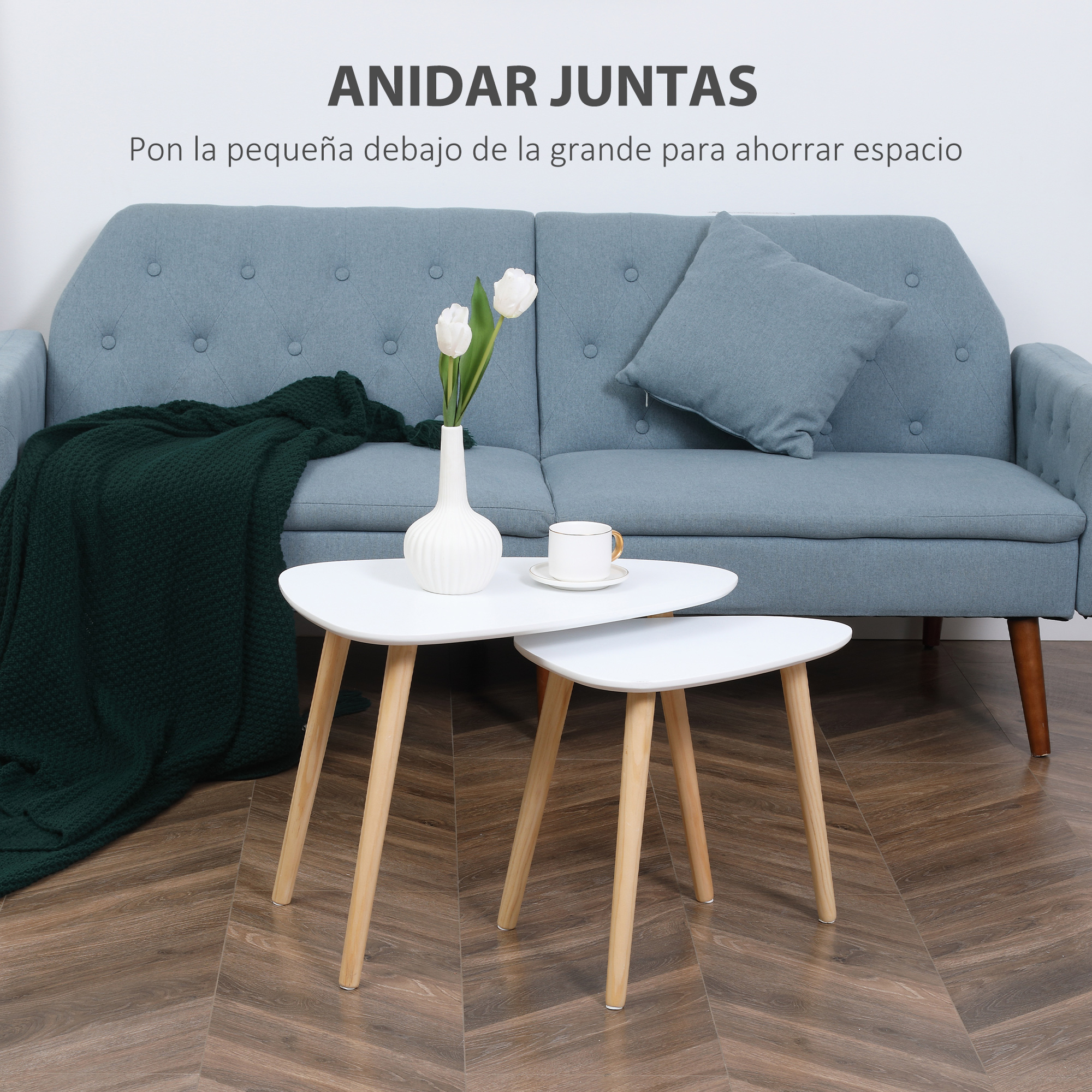 Un sofá azul con manta verde, tulipas blancas y dos mesas blancas.