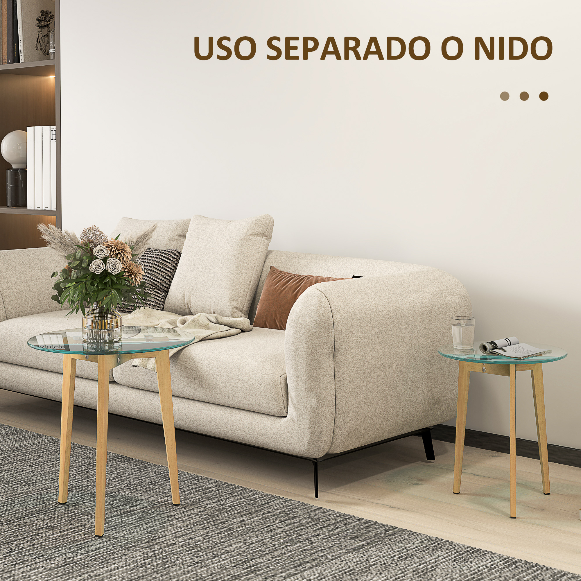 Una sala de estar con sofá, alfombra y dos mesas redondas de cristal, una con flores, otra con un vaso.