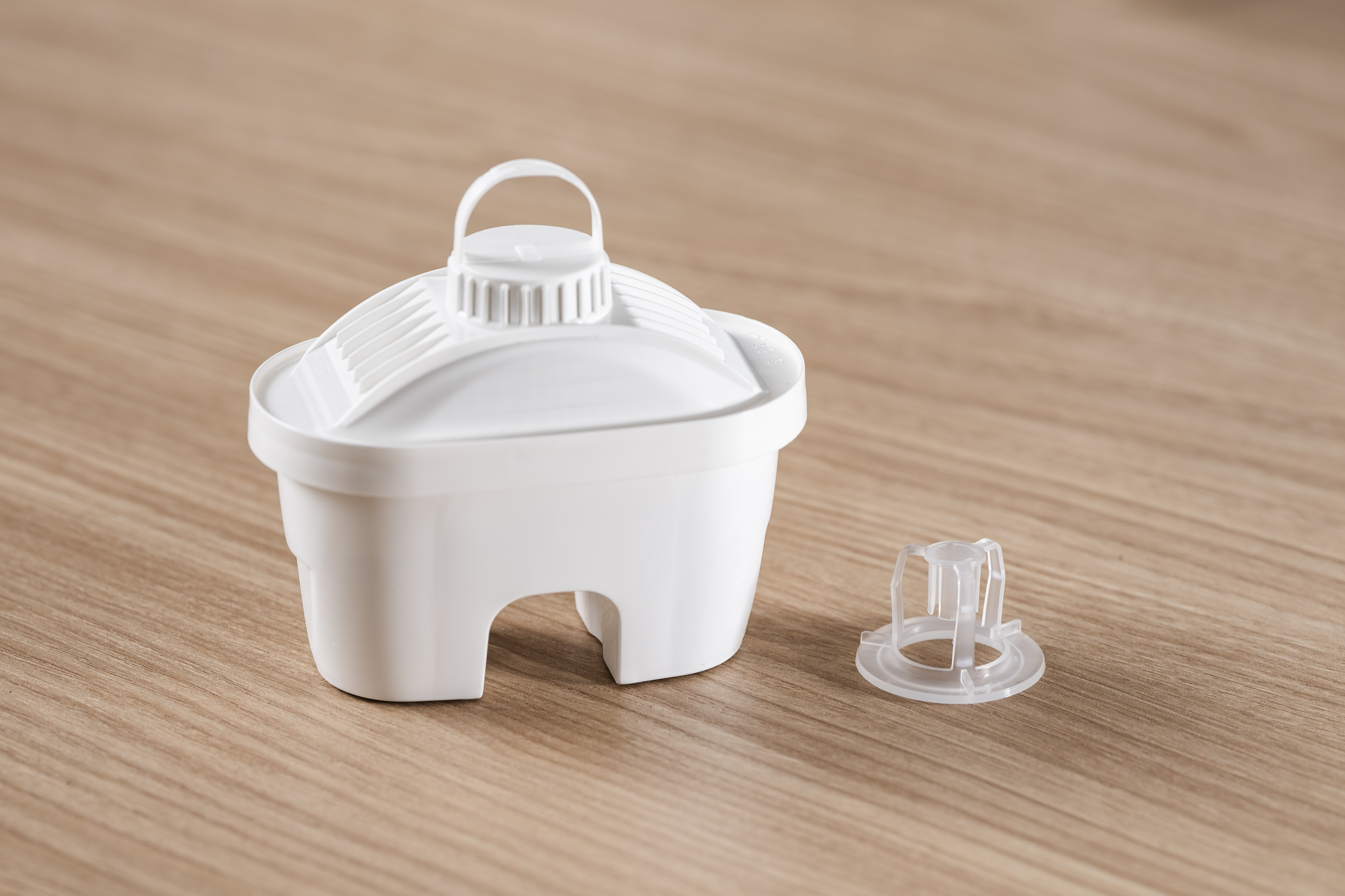 Biała obudowa wkładu filtra wody z osobną przezroczystą wkładką na drewnianym stole.