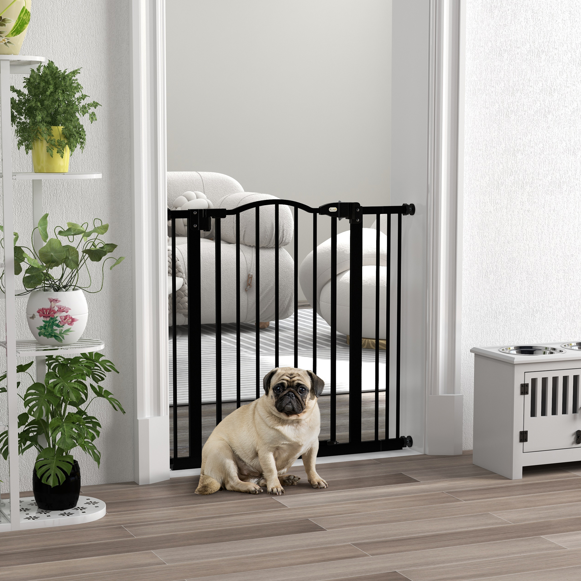 Un pug se sienta frente a una barrera para bebés negra en una habitación con plantas.