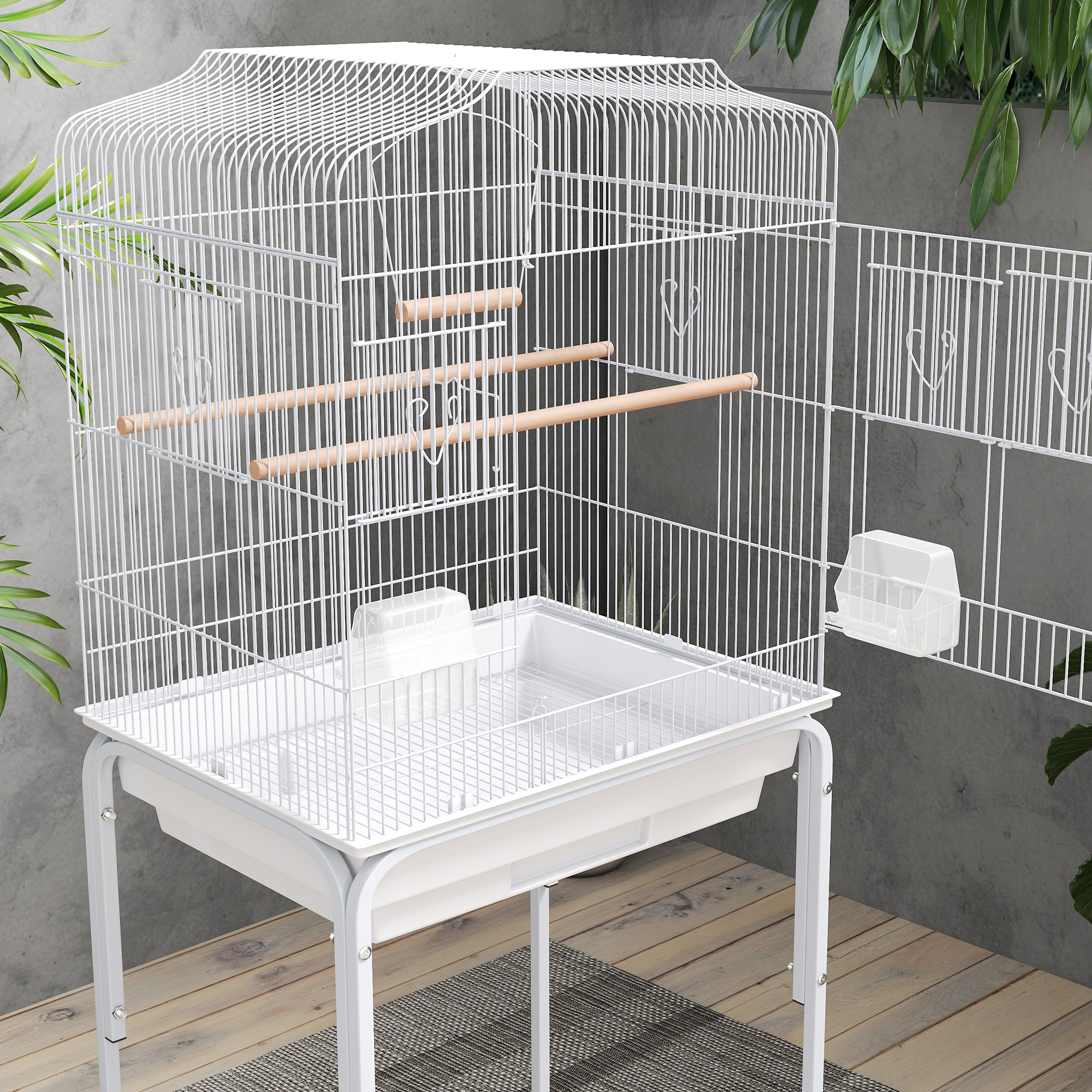Una jaula blanca para pájaros con perchas y comedero sobre suelo de madera.