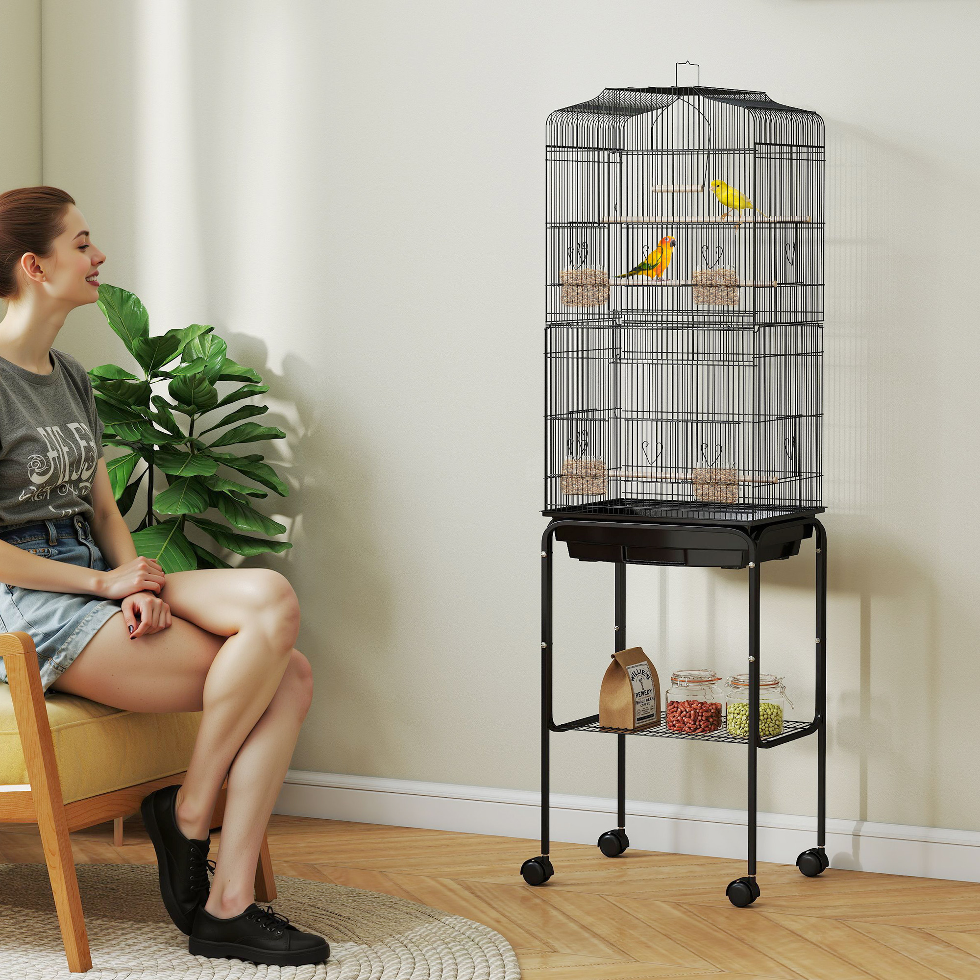 Una mujer sentada en una silla amarilla junto a una jaula alta para pájaros con dos pájaros.