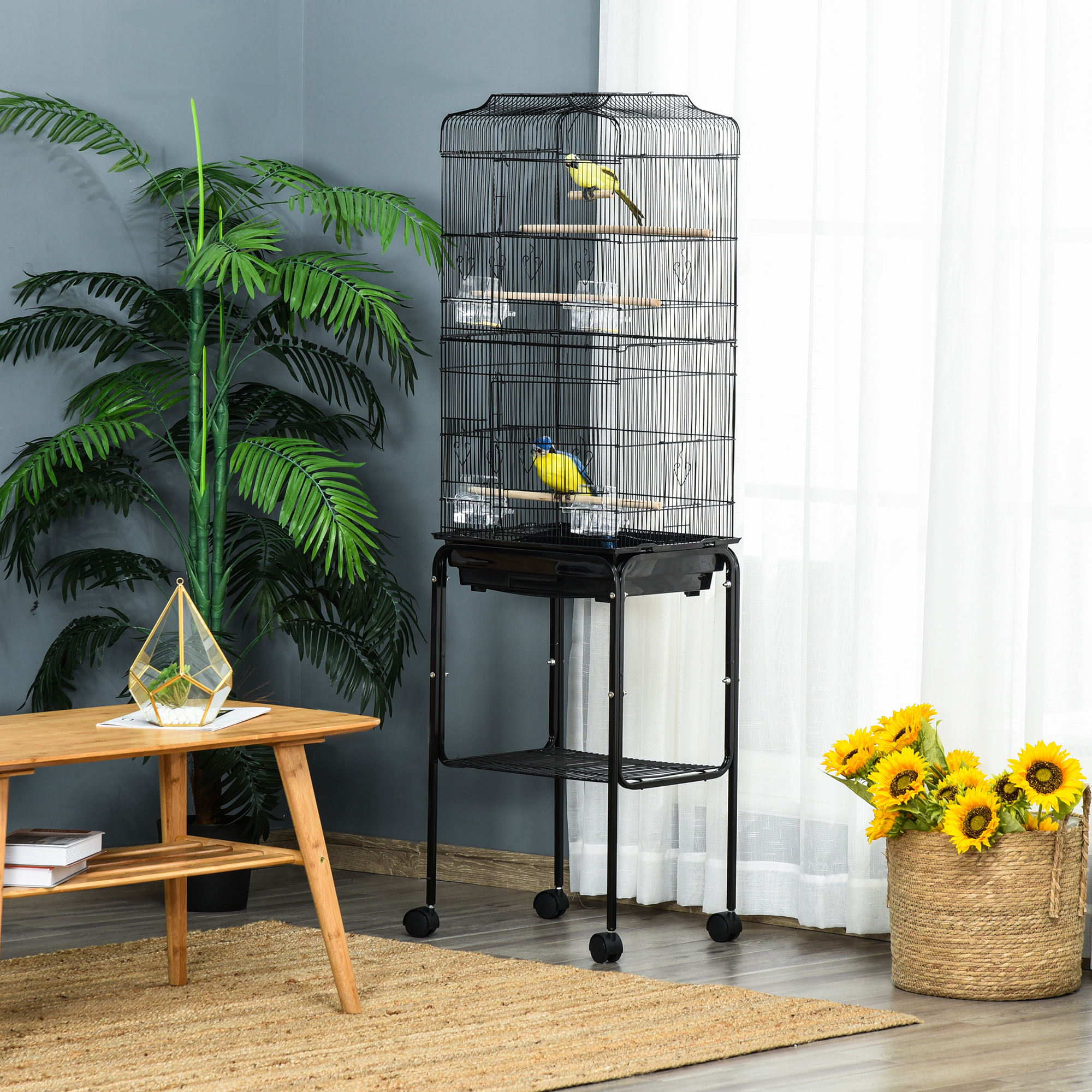 Una jaula negra para pájaros con dos pájaros y plantas junto a una mesa de madera con decoración.