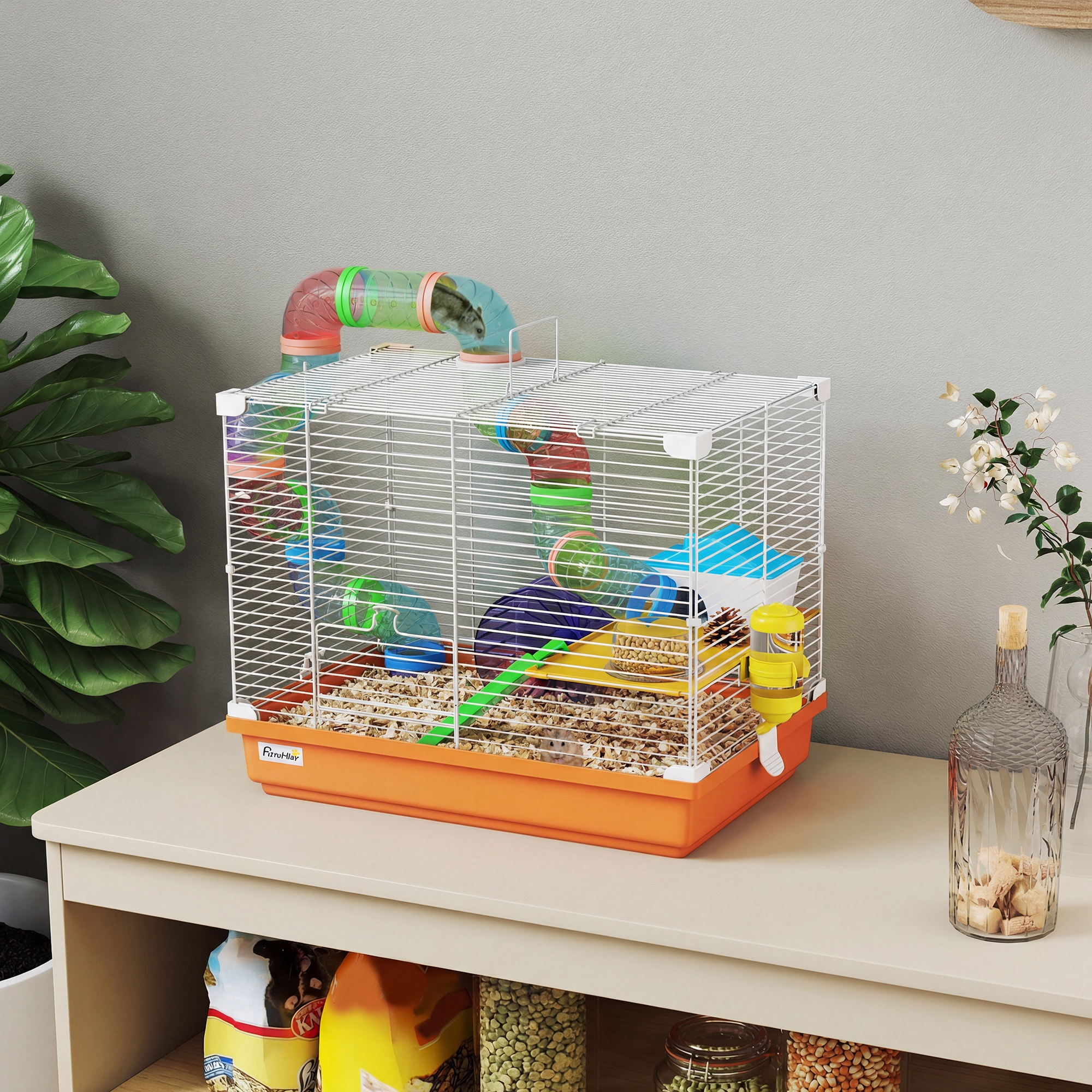 Una jaula de hámster con tubos y accesorios sobre una mesa. Una planta a la izquierda.
