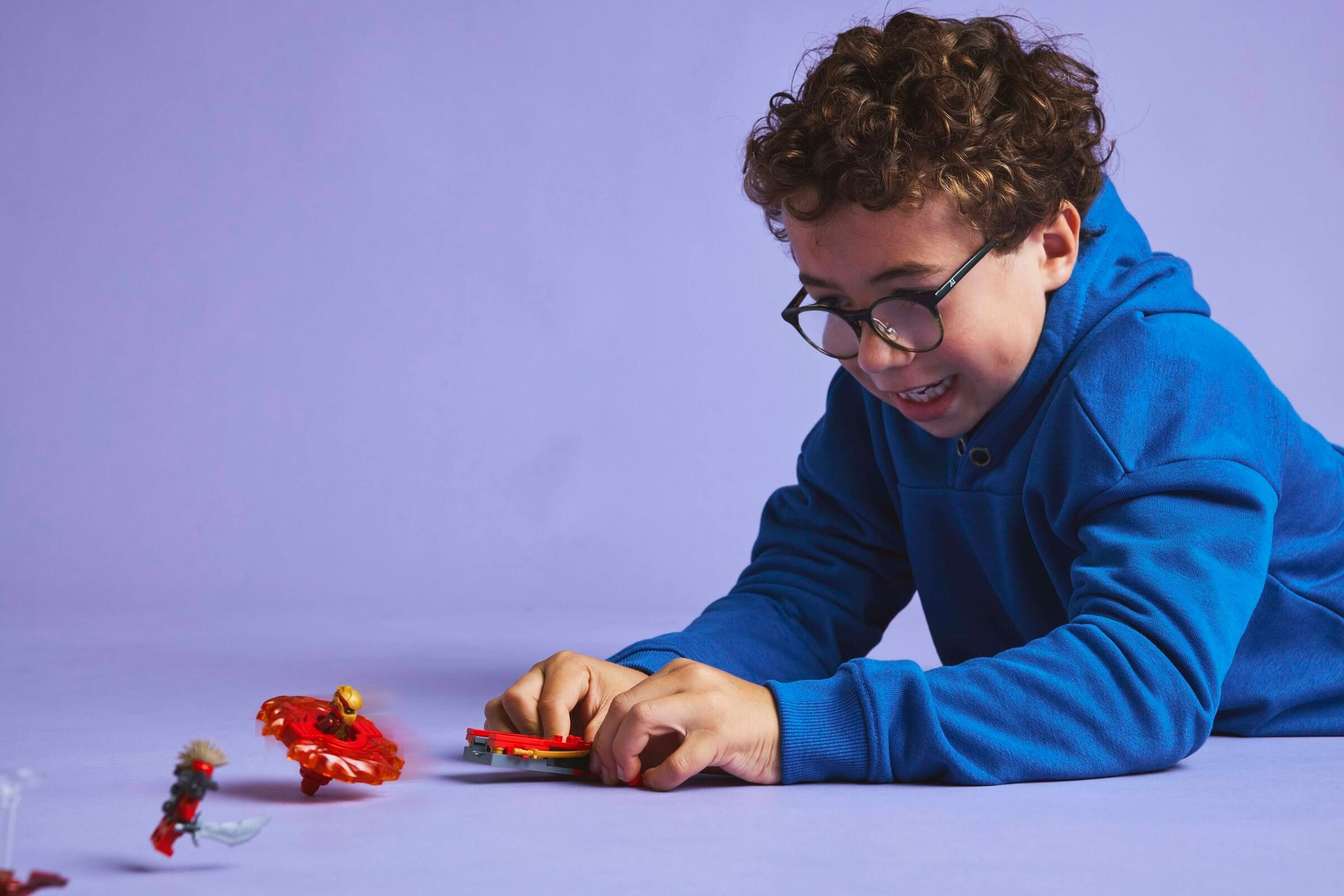 Ein Junge mit Brille spielt mit Spielzeugfiguren auf lila Untergrund.
