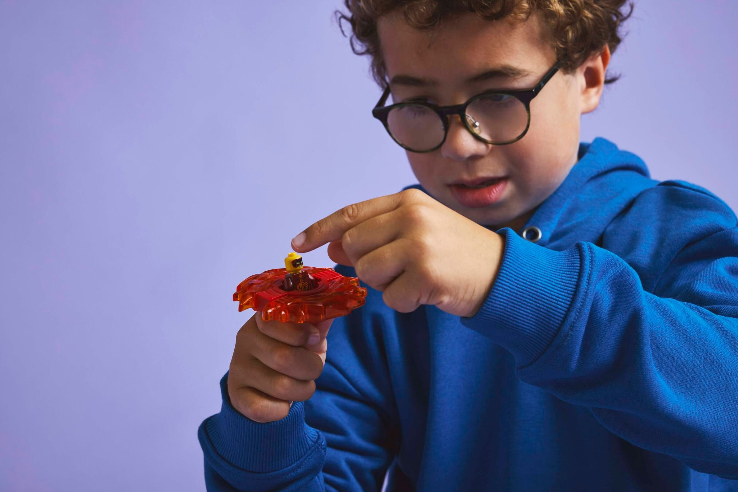 Ein Junge mit Brille hält einen roten Kreisel mit einer Lego-Figur.