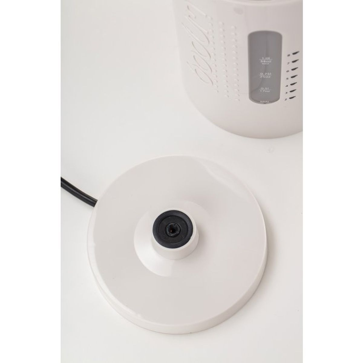 Un hervidor eléctrico blanco con cable negro sobre superficie blanca.