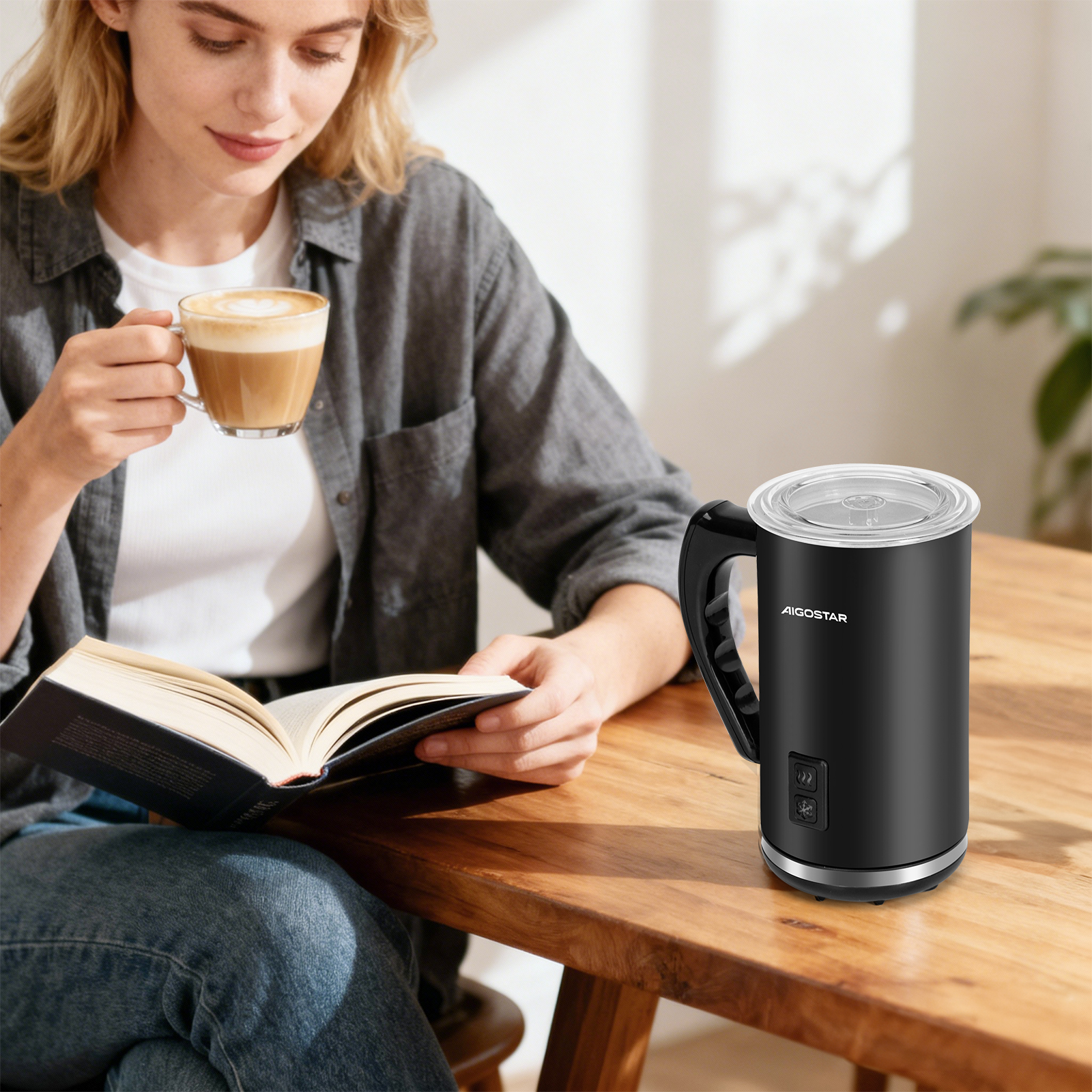 Frau liest Buch, trinkt Kaffee neben schwarzem Milchaufschäumer auf Holztisch.