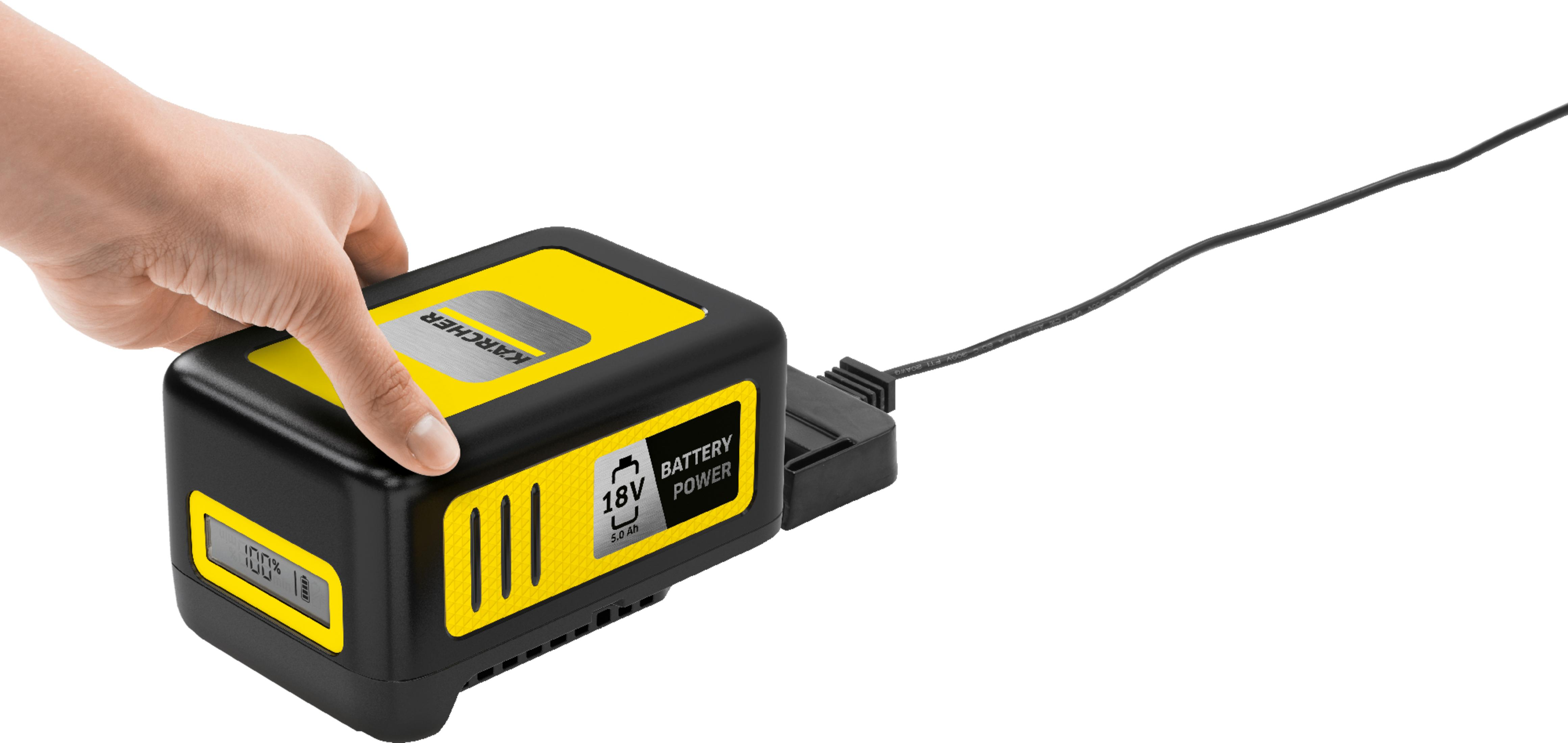 Eine Hand schiebt eine gelbe 18V Kärcher Akku-Einheit in ein Ladegerät.