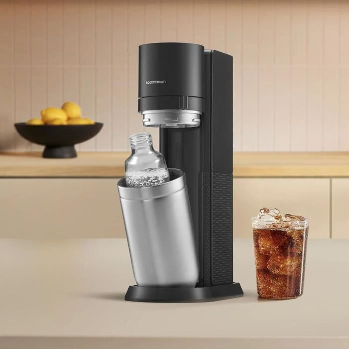 Ein schwarzer Sodastream mit einer Flasche und einem Glas Eistee daneben.