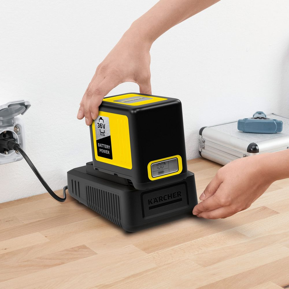 Osoba umieszcza żółtą baterię Kärcher na ładowarce.