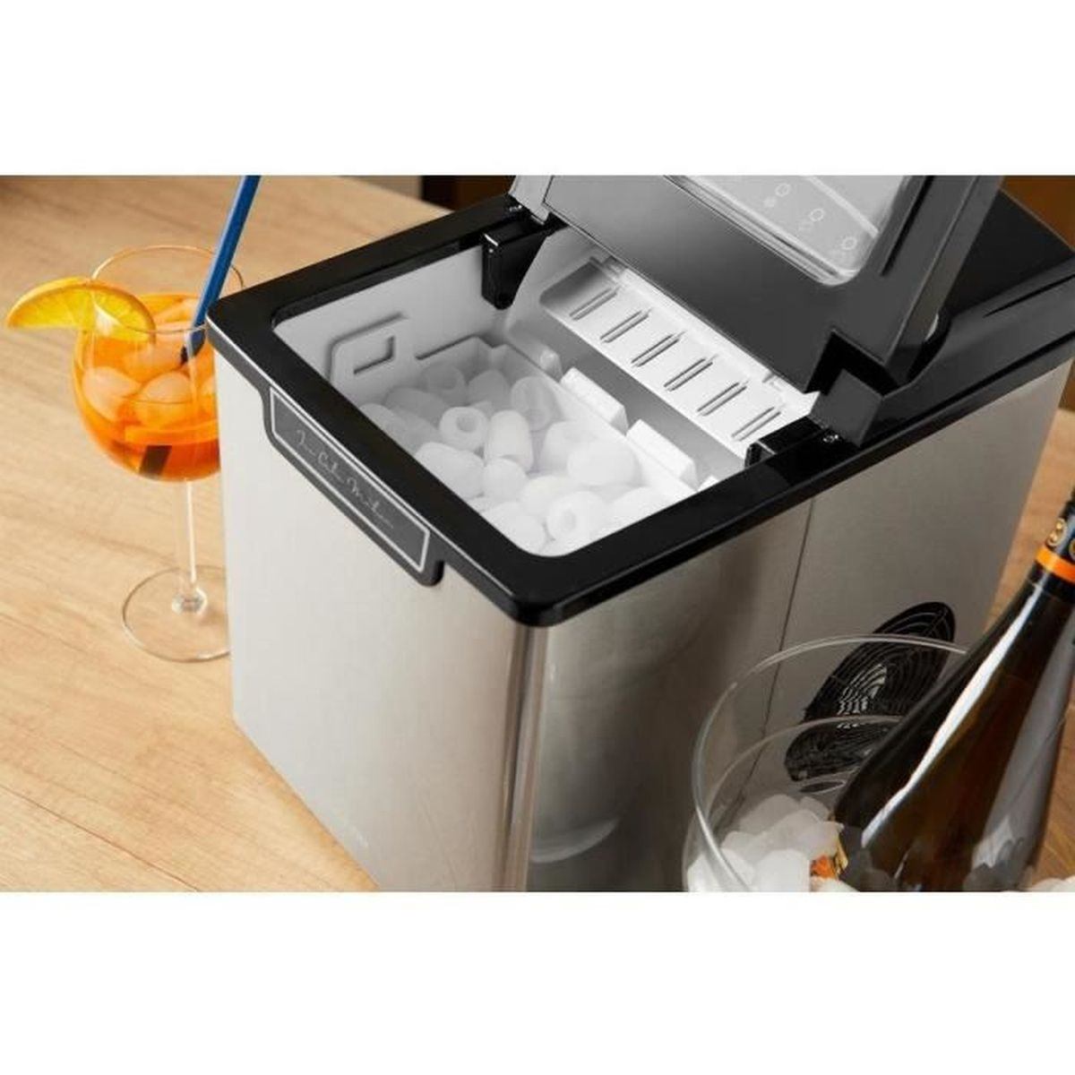 Una macchina del ghiaccio piena di cubetti di ghiaccio, accanto un bicchiere di Aperol Spritz e una bottiglia nel ghiaccio.