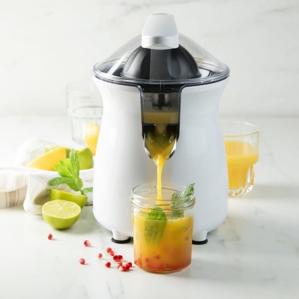 Un spremiagrumi bianco versa succo giallo in un barattolo con foglie di menta.
