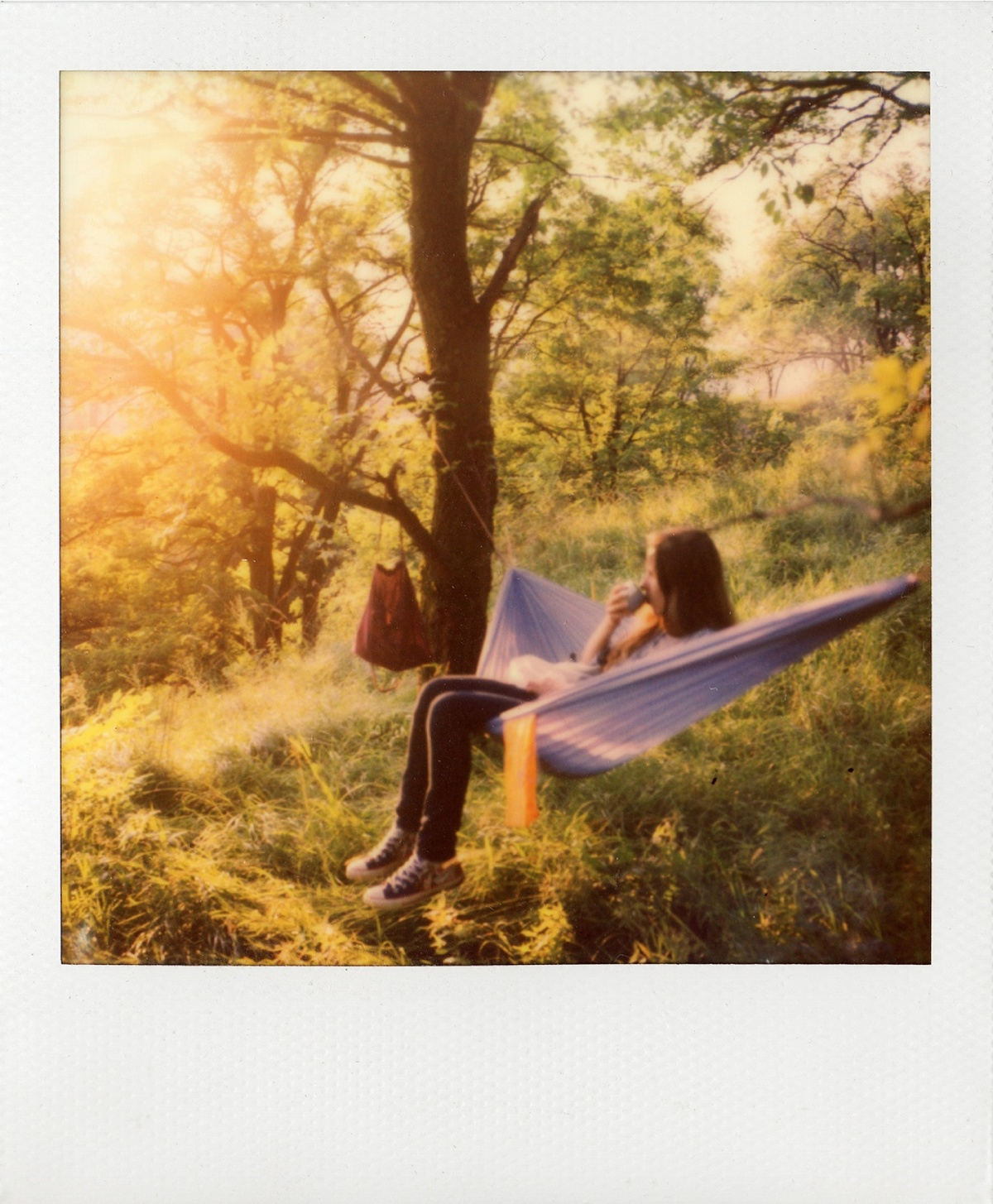 Una donna si rilassa in un'amaca all'aperto, tenendo una tazza. La luce del sole filtra tra gli alberi.