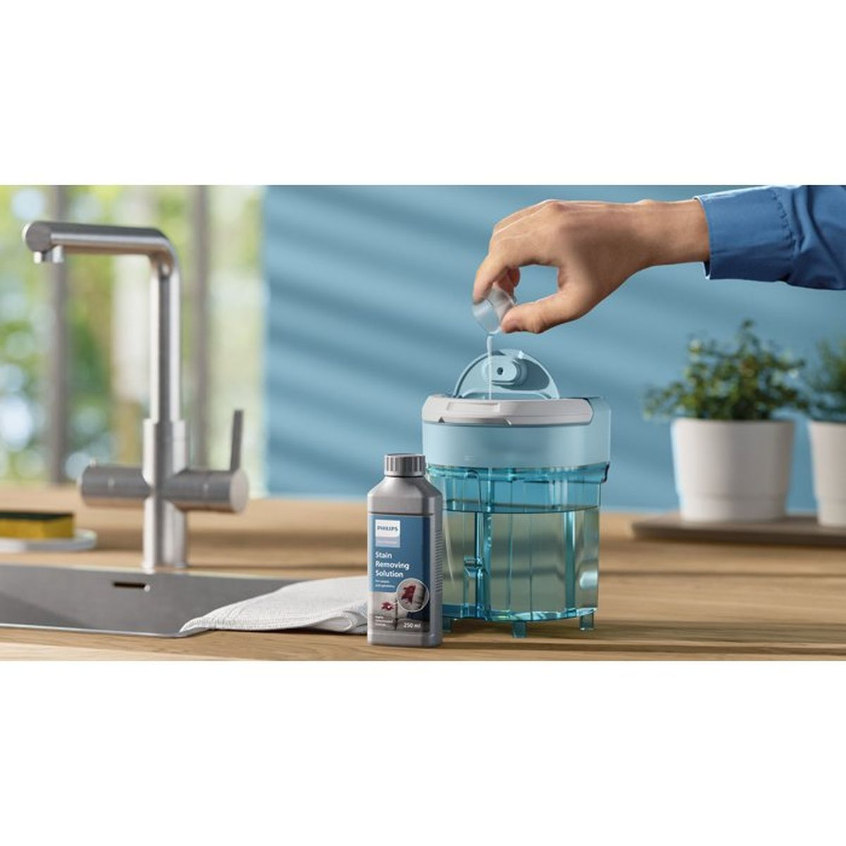Eine Hand gibt Flüssigkeit in einen blauen Behälter neben einer Flasche mit Fleckenentferner.