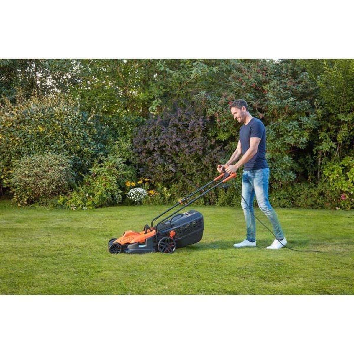 Hombre cortando césped con cortacésped naranja y negro en jardín frondoso.