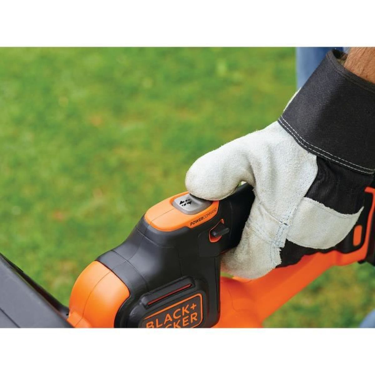 Eine Hand mit Handschuh bedient einen schwarzen und orangen Rasentrimmer über grünem Gras.