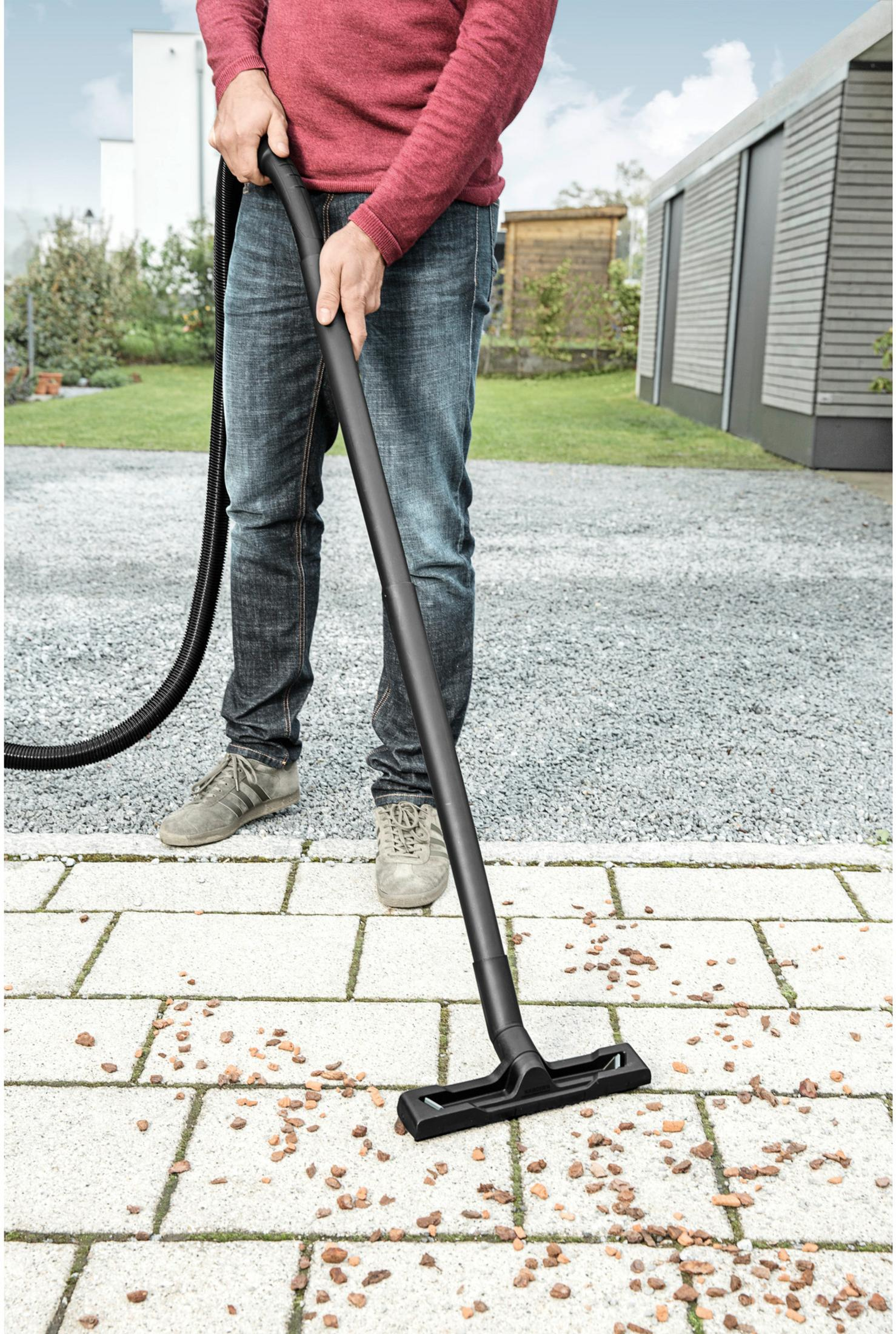 Homme aspirateur sur un chemin pavé avec tuyau et buse noirs.