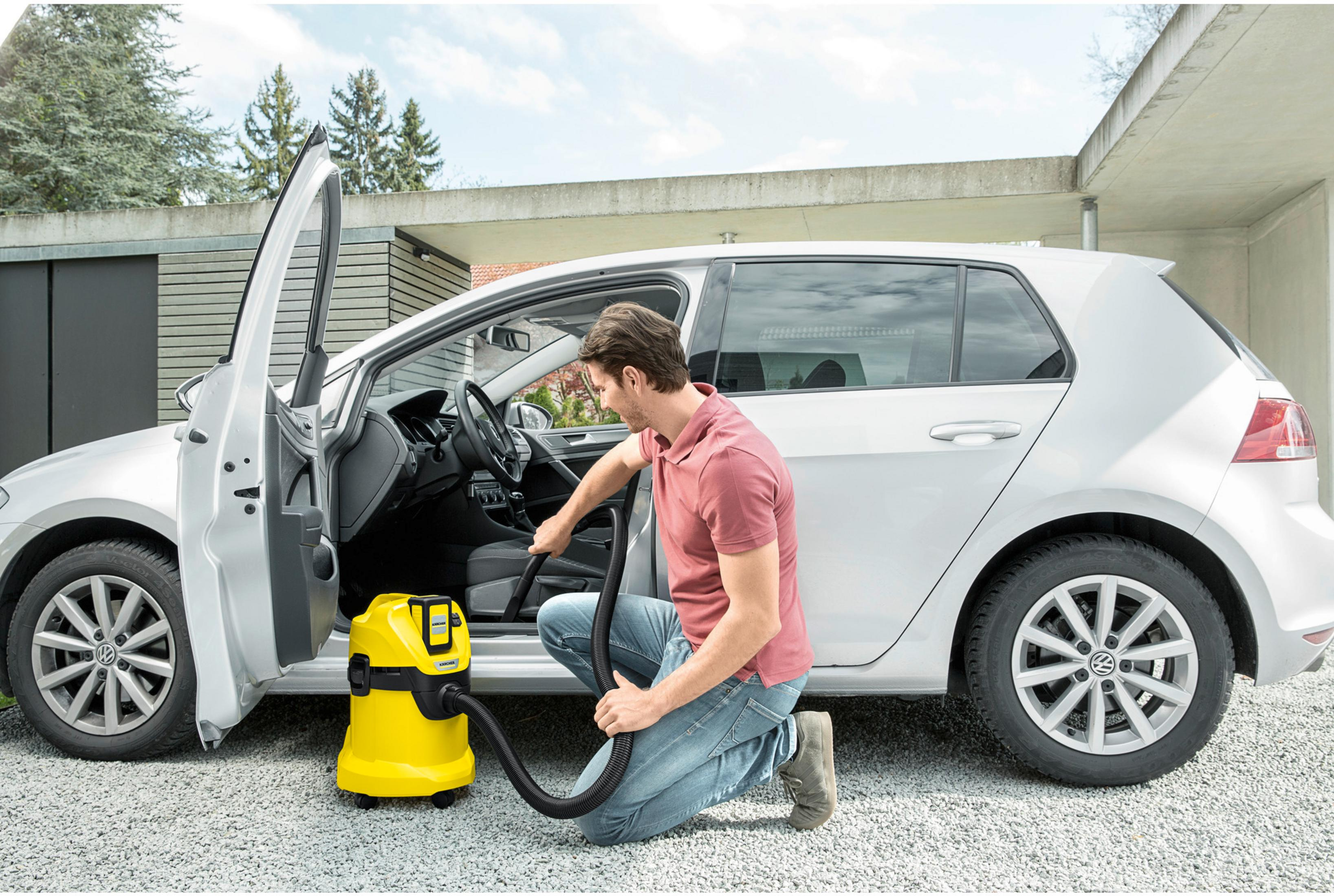Homme aspirateur intérieur de voiture avec aspirateur Karcher jaune. Voiture argentée, porte ouverte.