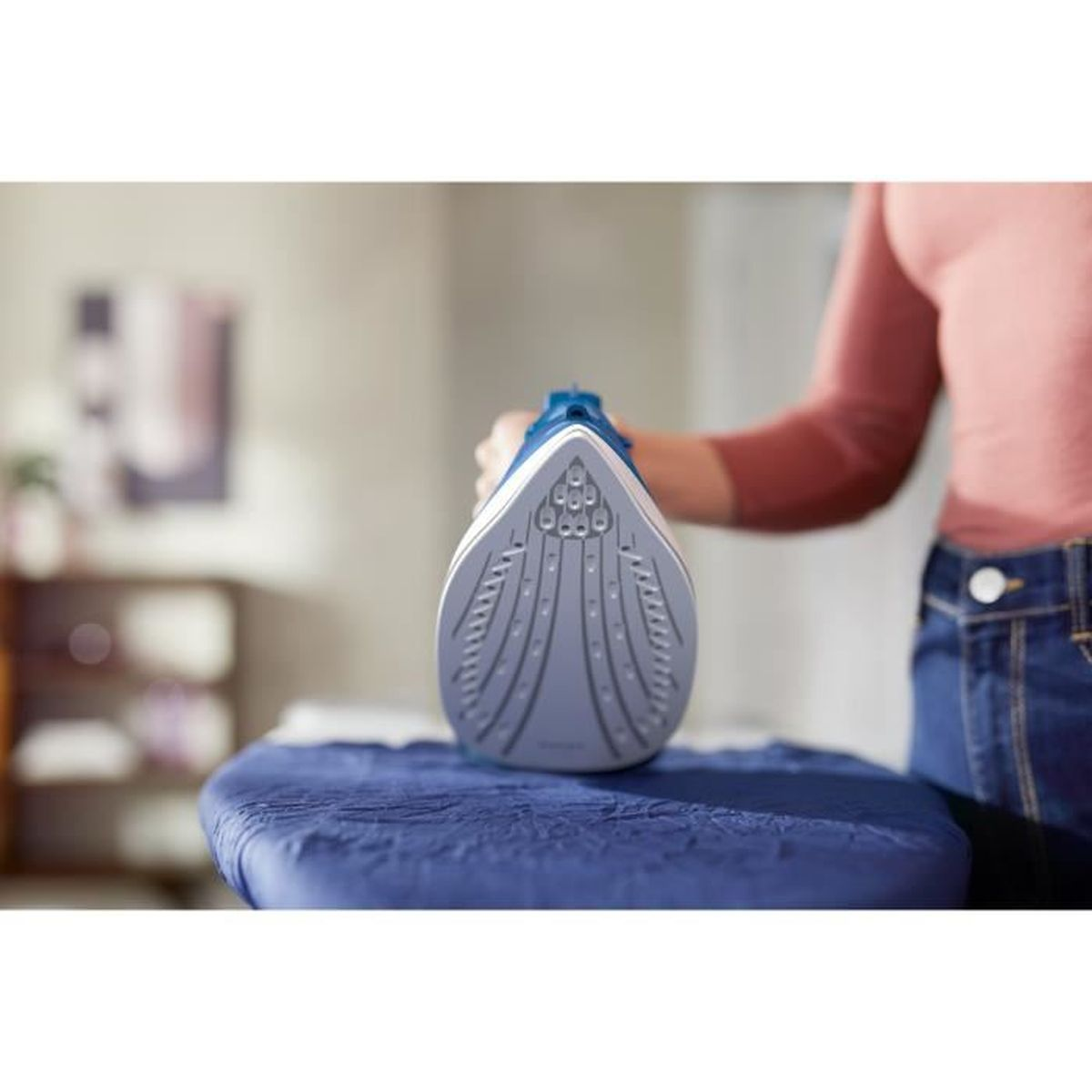 Osoba prasuje na niebieskiej desce do prasowania niebiesko-białym żelazkiem.