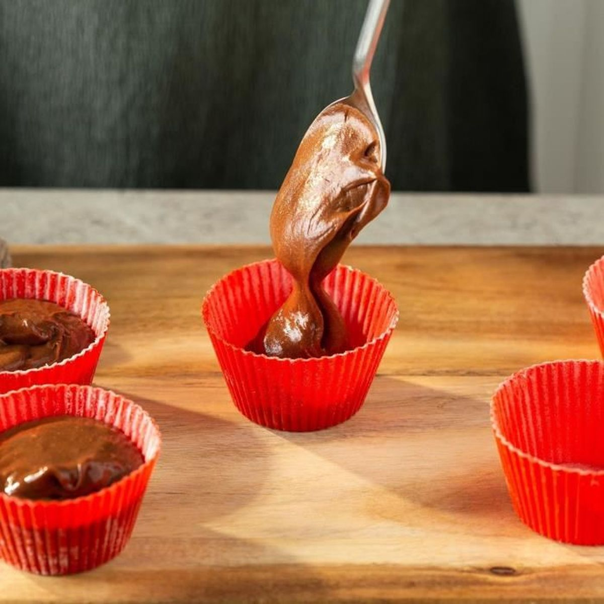 La masa de chocolate se vierte con una cuchara en moldes rojos para magdalenas.
