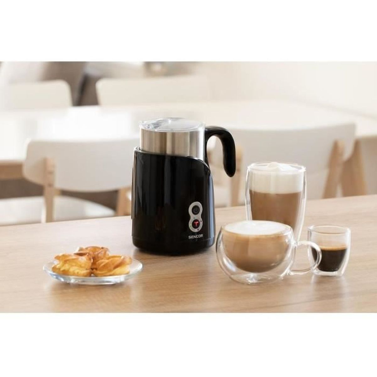 Ein schwarzer Milchaufschäumer mit zwei Tassen Kaffee und Gebäck auf einem Holztisch.