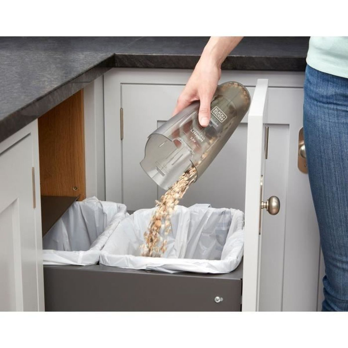 Ręka opróżnia przezroczysty pojemnik na brud do dwóch koszy na śmieci w kuchni.