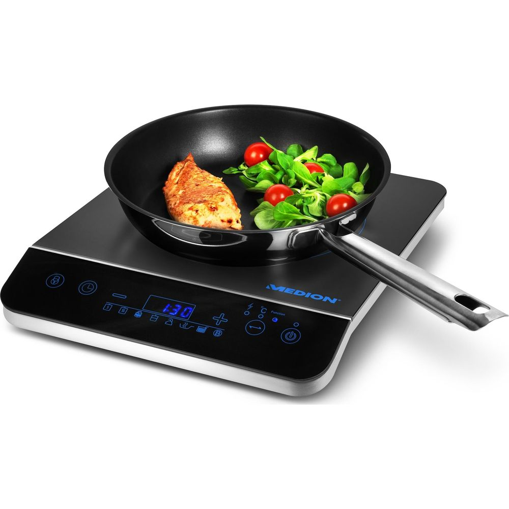 Kawałek kurczaka i sałatka są gotowane na patelni na płycie indukcyjnej.